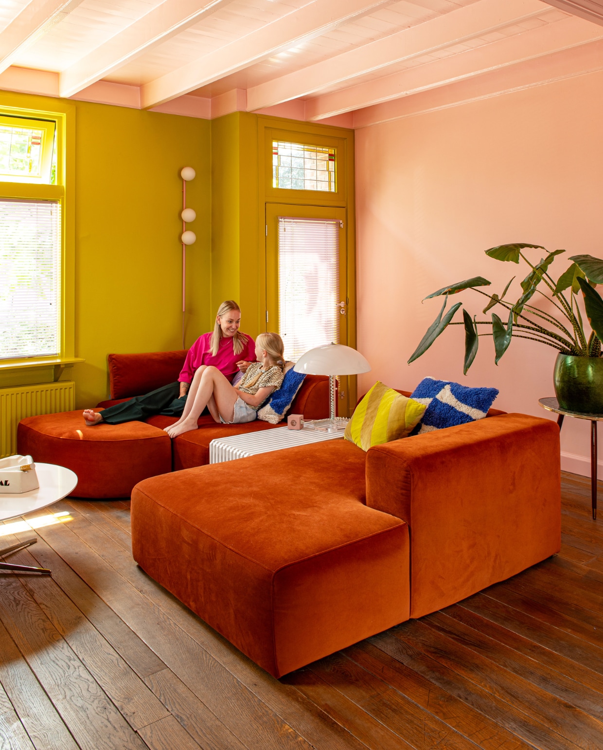 Bank 4x6 Sofa. Bijzettafel en geel kussen HKliving. Lamp Harco Loor, wandlamp Houseof, blauw-witte kussens H&amp;M, tafel uit Deense kringloop, asbak Seletti voor Diesel, plantentafel kringloop, pot lokale winkel. Roze verf wand en plafond Zalm en   geelgroene muurverf Wildernis van Gamma. vtwonen 11-2023 | productie De Binnenkijkers | styling Jeske Weel | fotografie Caroline Coehorst