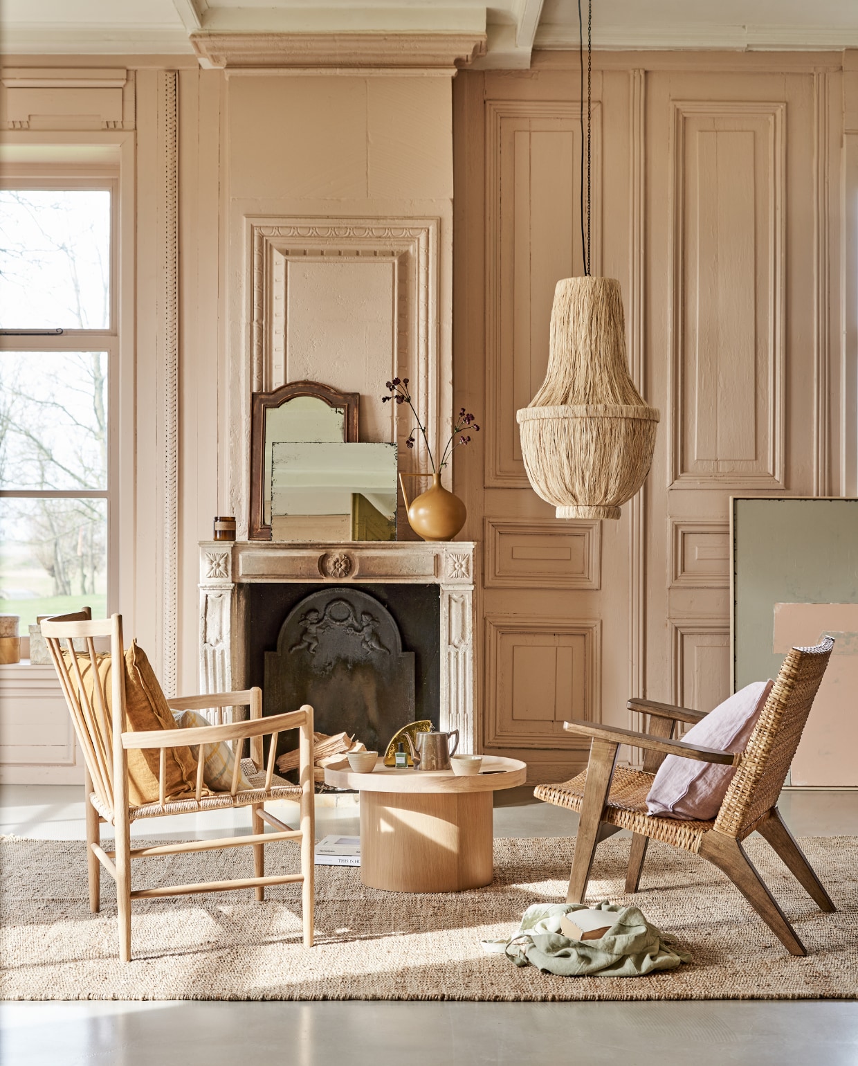 Fauteuil links FD Møbler J82 Jørgen Baekmark Lounge Chair vanaf € 1080,-, linnen tas € 37,90, geruit kussen€ 39,90, geurkaars € 27,90, mokken op tafel per stuk € 9,90 (letoile.store). Fauteuil rechts € 595,- vloerkleed, 200x300 cm € 349,-, kunstwerk Abstract 100x120 cm € 549,-, rechthoekige spiegel antieklook € 59,95, vaas in mosterdkleur € 47,95, glazen artwork op tafel € 59,95 (hkliving.nl). Zacht lila kussen van Bungalow € 47,-, okergeel kussen € 47,-, papieren dozen set van 2 € 36,- (scandicliving.nl). Oude spiegel met houten rand € 65,-(com-anders.nl). Salontafel Plateau van Bolia, 34,3x61 cm (hxØ) € 579,- (vtwonen.nl). Kroonluchter van gedroogde bananenbladeren € 599,- (rivieramaison.com). Kleur op de wanden vergelijkbaar met Setting Plaster No.231 van Farrow &amp; Ball. vtwonen 05-2021 | styling Marlies Does | fotografie Bart Brussee