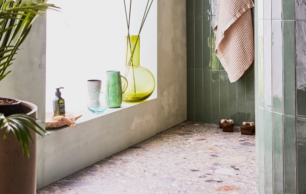 Donkere wandtegel Marrakesh kleur Army Green glans 6,5x40 cm, lichte wandtegel Marrakesh kleur Seagreen, glans 6,5x40 cm, vloertegel Composite kleur Multicolor 120x120 cm en badlakens van Marc O'Polo vtwonen.nl, planten pot nordal.eu, groene kan bungalow.dk, handzeep Meraki hm.com, grote groene glazen vaas hkliving.nl. Overig privébezit. vtwonen 08-2021 | styling Cleo Scheulderman | fotografie Jeroen van der Spek