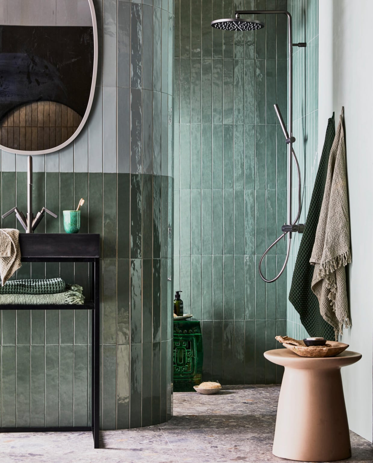 Lichte wandtegel Marrakesh kleur Seagreen glans, 6,5x40 cm, donkere wandtegel Marrakesh kleur Army Green glans, betonnen wastafel Tank met kraangat kleur Concrete Black, metalen frame kleur Black, planchet Frame kleur Oak Black, wastafelkraan Grip kleur Black Steel met twee hendels vtwonen.nl, spiegel van Umbra, badlakens van Marc O'Polo, beker, lichtgroene wafeldoek, grijze gastendoek bungalow.dk, keramieken kruk polspotten, handzeep Meraki H&M. vtwonen 08-2021 | styling Cleo Scheulderman | fotografie Jeroen van der Spek