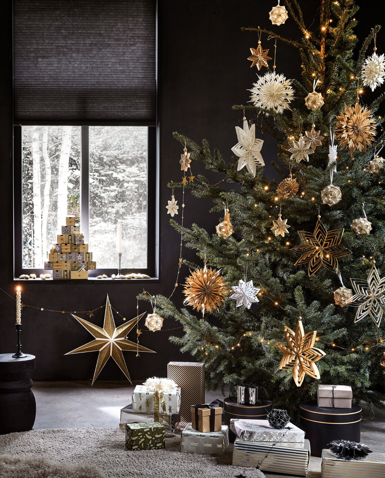 Kartonnen adventskalender € 27,99, goudkleurige kaars met glitter, per 2 € 6,99, goudkleurige papieren ster, 70x19 cm (Øxd) € 9,99, goudkleurige slinger met sterren, 210 cm (l) € 3,49 (ook verkrijgbaar in zilver). In de boom: diverse papieren ornamenten in de kleuren goud, wit, zilver en zwart, per stuk vanaf € 2,49, zilverkleurige lichtslinger warm wit met 30 ledlampjes op batterijen inclusief display en timer, 300 cm (l) € 3,99.M.m.v. karwei.nl (zwarte kandelaar, taupe schapenvacht, zwarte houten kruk Bikkel, taupe schapenvacht), hema.nl (inpakpapier), janvanvulpenboomkwekerij.nl (kerstboom). vtwonen 12-2022 | productie Tanja Saarberg, Isa Hoevens | styling Kim van Rossenberg | fotografie Peggy Janssen