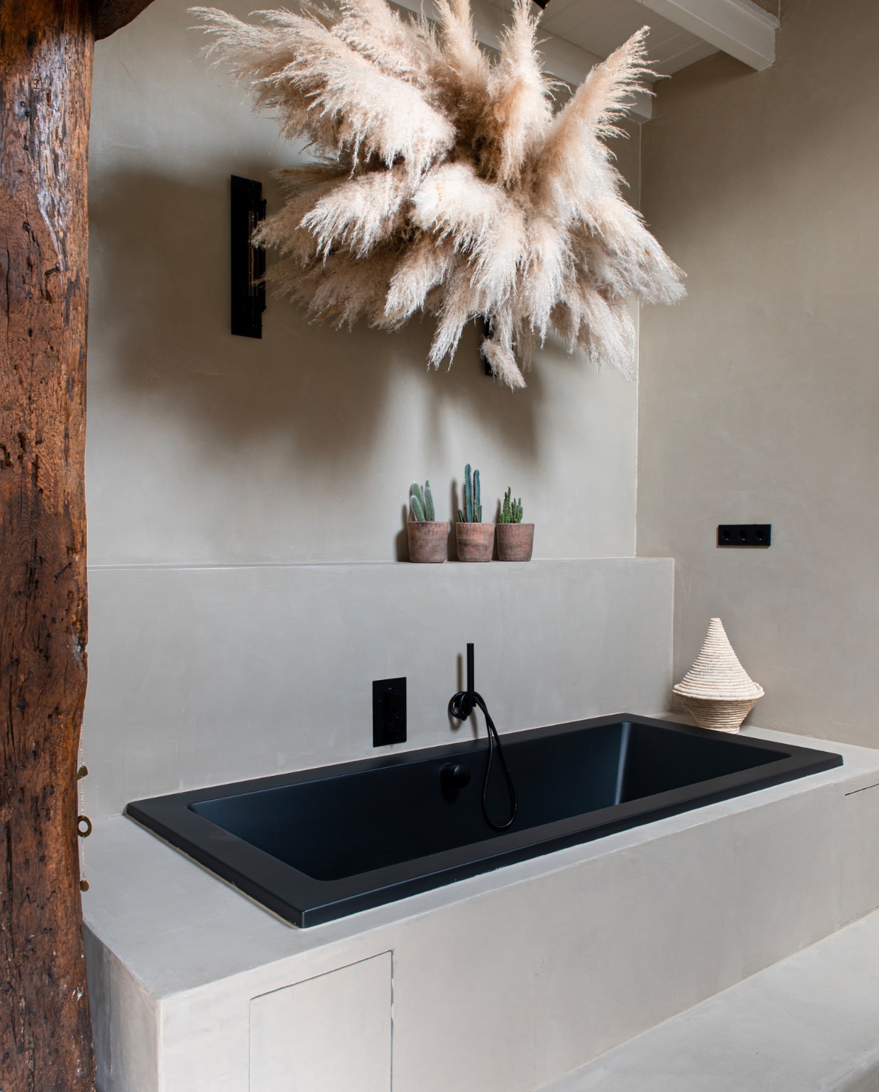 Bad en kraan Voortman Pesse. Ombouw zelfgemaakt en afgewerkt met beton ciré. Potten Bloem &amp; So, pluimen Maison Aimélie, rieten mand Mi-Casa. vtwonen 11-2023 | productie De Binnenkijkers | styling Jeske Weel | fotografie Caroline Coehorst
