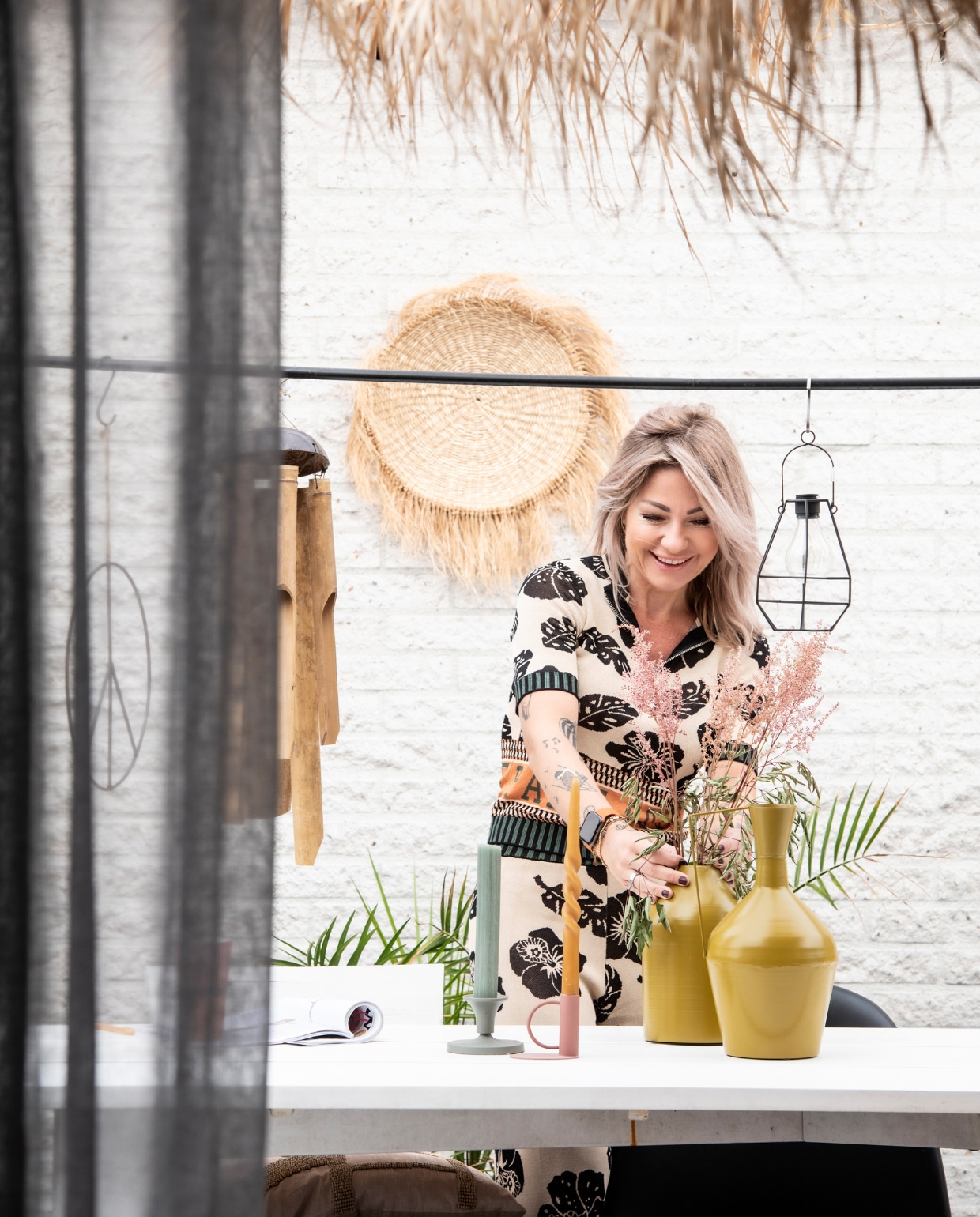 Parasol J-Line, rieten wanddecoratie Mars &amp; More, tafel vtwonen, varen BePureHome, peaceteken Evenaar. Kandelaars Branded, kaarsen Ravie en Rustik, vazen BePureHome, draadlamp Intratuin, bamboehanger Tica. vtwonen 3-2022 | productie Insidehomepage | styling Esther Loonstijn | fotografie Louis Lemaire