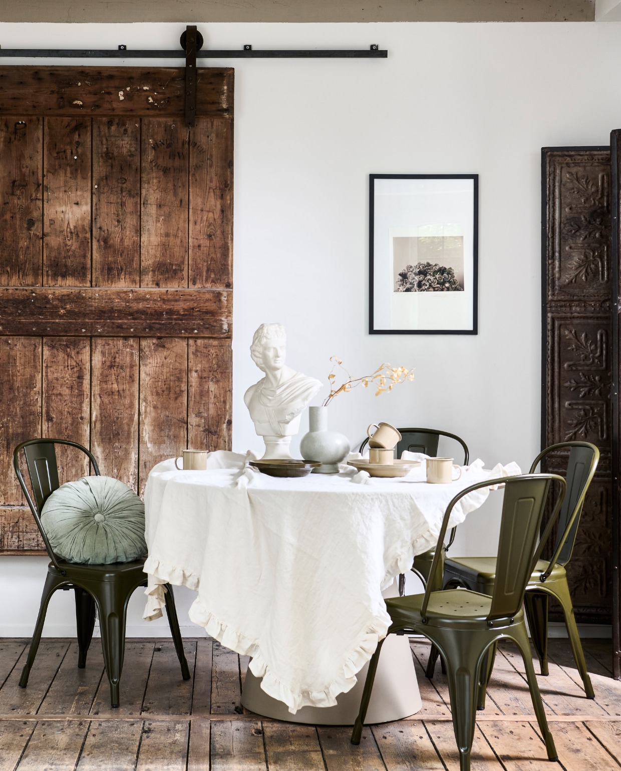 Mdf eettafel Jorre van Woood in Militair Brown, 120x76 cm (Øxh) € 499,-, ijzeren stoel Afternoon van vtwonen € 99,95, porseleinen vaas Tank van BePureHome € 39,95, velvet kussen Halo van BePureHome € 29,95 (basiclabel.nl). Metalen kamerscherm van oude plafonddecoratie, 188x2x194 cm (lxbxh) € 495,- (hetkabinet.nl). Vintage borstbeeld € 98,- (fortuneflea.com). Bekers en borden uit serviesset Picnic in kleur Cashmere van Ferm Living 8-delig € 79,-, metalen borden uit picknickset Yard Picnic van Ferm Living in Cashmere en Olive € 79,- (vtwonen.nl/shop). Linnen tafelkleed met ruche en kunstwerk privébezit. vtwonen 11-2023 | styling Marlies Does | fotografie Sjoerd Eickmans
