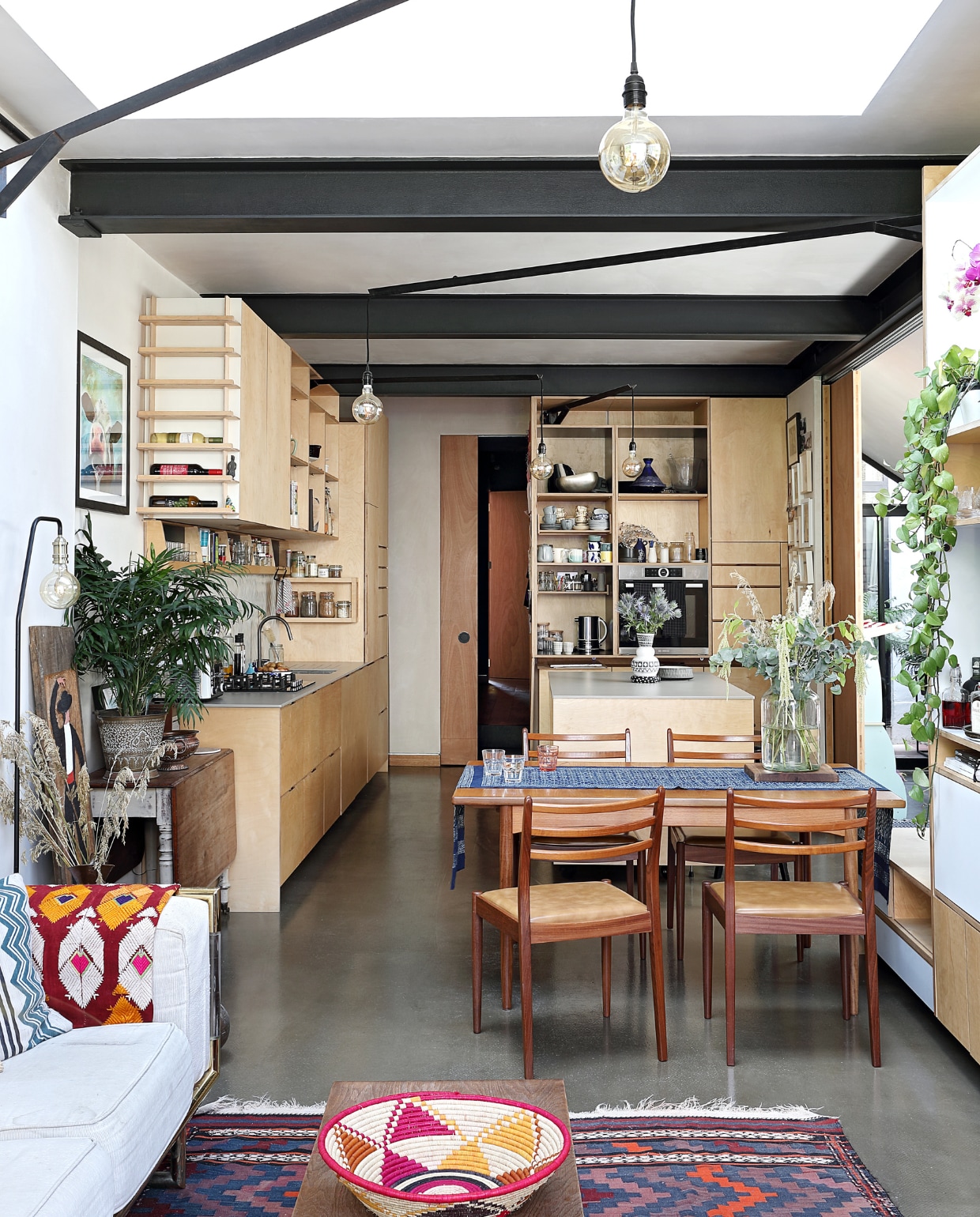 Voor een ruimtelijk effect kwam er een open keuken, maar wel met een schuifdeur. Mallika: ‘Als we die dichtdoen, ontstaat een logeerkamer in de zijaanbouw.’ Tafel en stoelen Sunbury Antiques Market, tafelkleed uit Pakistan. Vintage bijzettafel en plantenpot Kempton Park Market. Kunstwerk met koe van Charlotte Gerrard. Bank gekregen, mand HomeSense, kleed van een kringloop.  vtwonen special binnenkijken 03-2020 | productie Bureaux | styling Someday Studio | fotografie Elsa Young