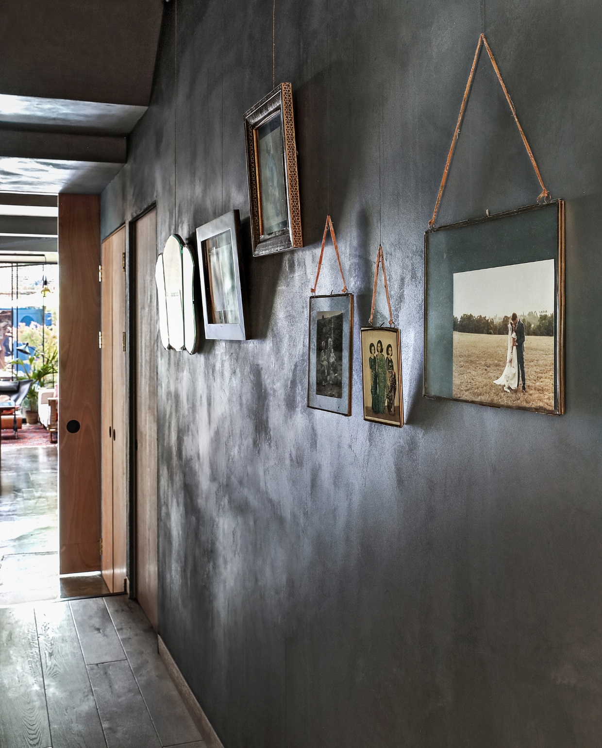 In de gang zijn de muren bewerkt met klei van
Clayworks. Mallika: ‘De donkere kleur is speciaal voor
ons samengesteld, wij noemen het walvisgrijs.’ Aan de
muur ingelijste familiefoto’s en vintage spiegels. vtwonen special binnenkijken 03-2020 | productie Bureaux | styling Someday Studio | fotografie Elsa Young