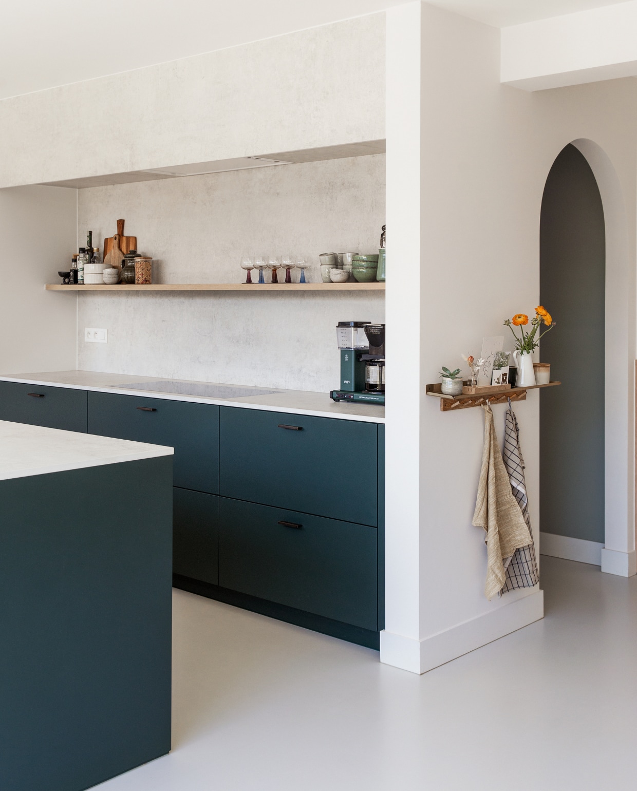 Keuken Raeymaekers Keukens, kleur keuken Carriage Green Farrow & Ball, keukenblad Dekton in Lunar, verlichting Modular, koffiezetapparaat Moccamaster. Kommen, theedoek en snijplanken Casa. Theepot en vaas tweedehands. Gouden wandplank La Redoute, kapstok H&M, andere theedoek Ferm Living, kaars HKliving, kaarthouder Tiny Glory, gietvloer kleurcode NCS S2000N van Alterieur. Overig onbekend.
