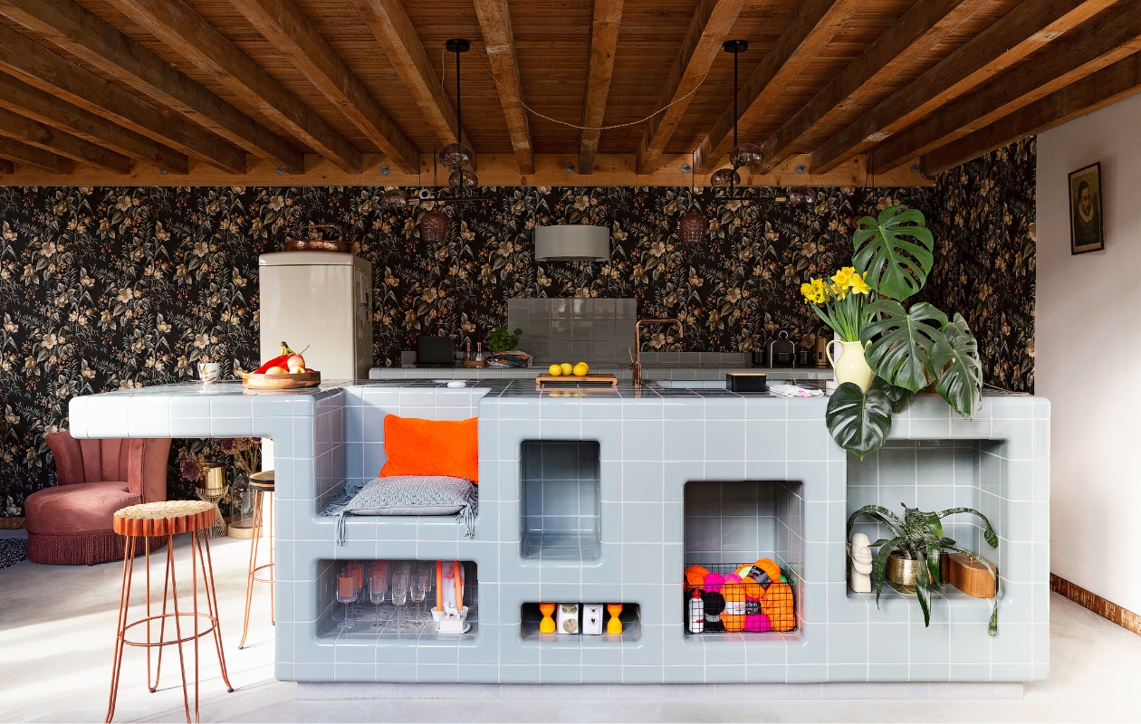 Dtile keuken zelfgemaakt. Kraan Nivito. Houten groenteschaal Hema. Snijplank Ikea. Dutchbone fauteuil Loods 5 Garage. Barkrukken Kave Home Farley. Hanglampen Made.Koelkast M-system. Afzuigkap, apparatuur en inductieplaat Ikea. Natuurbehang Hornbach. Overig onbekend. vtwonen 10-2021 | styling Emmy van Dantzig | fotografie Jansje Klazinga