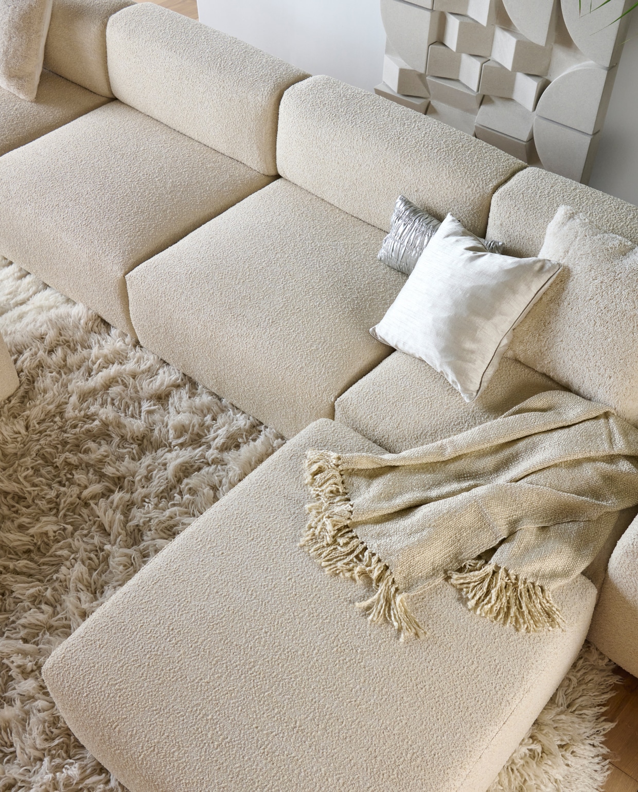 Elementenbank Cubi Spacious en poef Large, allebei van Basta in Linen Melé  (basta.co). Hoogpolig vloerkleed Fluffy, wol en katoen, 250 cm (Ø) (hkliving.nl). Wandpaneel Montañas, 175x100 cm (lanena-home.com). Acryl plaid Solid van Malagoon in Ivory (vtwonen.nl/shop). Wollen kussen Tufted Solid (malagoon.com). Zilveren katoenen kussen New Age van HKliving (loods5.nl). Zijdeglanzend kussen (nordal.com). vtwonen 11-2023 | Styling Marianne Luning | Fotografie Sjoerd Eickmans