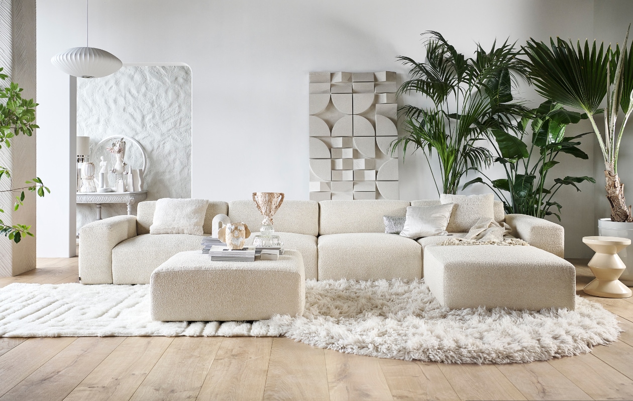 Elementenbank Cubi Spacious € 4420,- en poef Large € 610,-, allebei van Basta in Linen Melé  (basta.co). Houten parket XL in geolied eiken white wash van vtwonen, per m2 € 94,95, muurverf krijtlook Snow White van vtwonen, per 2,5 liter € 46,99 (karwei.nl). Hoogpolig vloerkleed Fluffy, wol en katoen, 250 cm (Ø) € 1575,- (hkliving.nl). Wollen vloerkleed van Brinker Carpets, hoog- en laagpolig, 200x290 cm € 1250,- (eijerkamp.nl). Wandpaneel Montañas, 175x100 cm € 1249,- (lanena-home.com). Polyester bijzettafel Zig Zag van Polspotten € 345,-, hanglamp Nelson Saucer Bubble van Hay € 695,-, acryl plaid Solid van Malagoon in Ivory € 49,95, aardewerken vaas Moire van Ferm Living € 139,- (vtwonen.nl/shop). Wollen kussen Tufted Solid € 59,95 (malagoon.com). Zilveren katoenen kussen New Age van HKliving, € 49,95, porseleinen gebouwen van Joost Gijzel, per stuk € 79,- (loods5.nl). Zijdeglanzend kussen € 50,-, aardewerken plantenpot € 225,- (nordal.com). Marmeren boekensteun Ferro van Nordal € 68,- (deens.nl). Tweedehands wandtafel € 100,-(delokatie.nl), geverfd in hoogglans lak White Wood nr. 201 van Lab Paint, 500 ml € 47,- (vestingh.nl). Kunstobjecten, aardewerk en gerecyclede materialen, vanaf € 150,- (vazenvanjanssen.nl). Gipsen cirkel € 85,-, venusbeeld € 59,90 (het-schippertje.nl). Overig privébezit. vtwonen 2023-11 | styling Marianne Luning | fotografie Sjoerd Eickmans