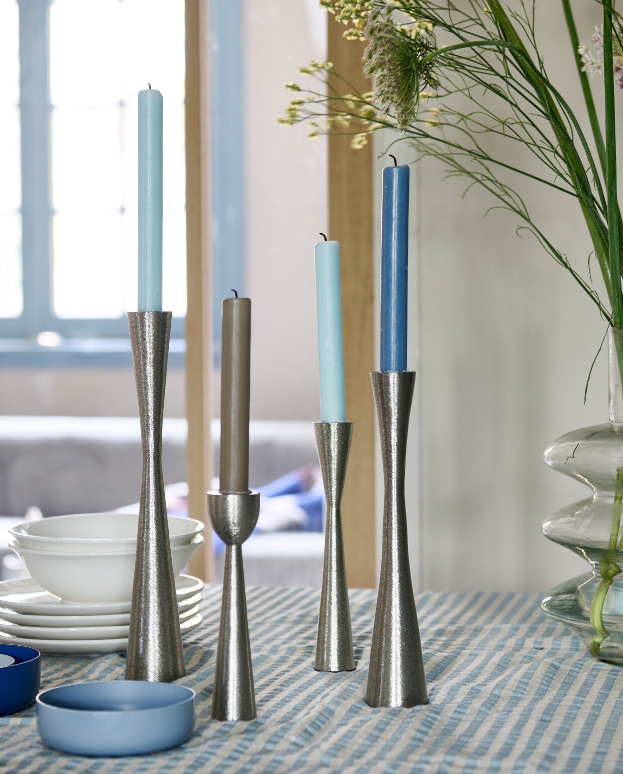 Kandelaars vanaf € 16,95. Servies wit, losse onderdelen vanaf € 1,95. Vaas van helder glas € 44,95.M.m.v. zarahome.com (tafelkleed), hm.com (blauwe bakjes). Overig privébezit. vtwonen catalogus 2023