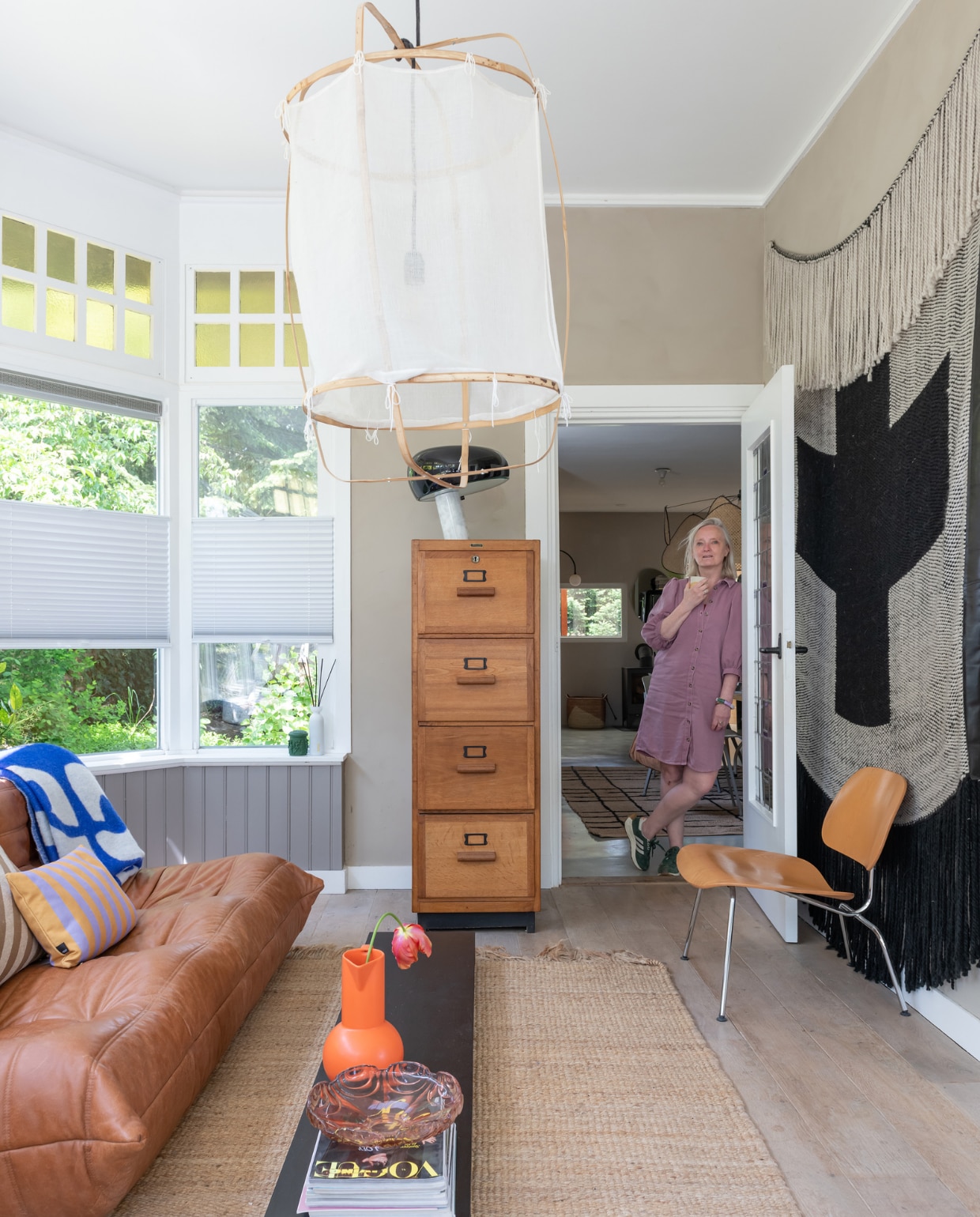 Wilma in de woonkamer van haar vrijstaande huis. Betonlook verf Biscuit van Betonstunter, vloer Marktplaats. Vintage bank Togo van Ligne Roset, plaid Arket, gestreept kussen Fést, vloerkleed HKliving. Salontafel zelfgemaakt, glazen schaal rommelmarkt, oranje vaas Raawii. Tweedehands ladekast Loods66, tafellamp Snoopy van Flos, hanglamp via Instagram @just_bysan, stoel Eames LCM van Vitra, wandkleed NADesign. vtwonen 12-2023 | styling Sharon Roest | fotografie Caroline Martinot