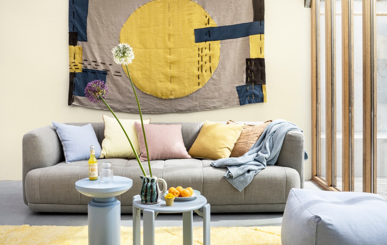 Ontwerp en realisatie wandkleed (cobo-co.nl), stoffen per meter vanaf € 20,- (boerenbonthal.nl). Op de muur zachtgele krijtverf Katoen, per liter € 8,95 (dullerenco.nl). Bank Quilton, 248x109x72 cm (bxdxh) vanaf € 3509,-, kruk Rey Stool € 465,- (hay.nl). Wollen vloerkleed, 180x280 cm € 1295,- (hkliving.nl). Lichtgeel en lichtblauw kussen Outline van Hay € 75,-, roze wollen kussen van Malagoon € 49,99, bijzettafel van Nordal € 239,-, poef van Hay € 249,-(vtwonen.nl). Terra linnen kussenhoes € 9,99 met kussenvulling € 14,99 (ikea.nl). Katoenen plaid € 109,- (bymolle.nl). Glazen vanaf € 1,25, keramieken kan € 33,- (serax.com). Bord € 12,50 (hetgroteavontuur.nl). Potje € 0,75, limonade (dille-kamille.nl). vtwonen 08-2022 | styling Marianne Luning | fotografie Stan Koolen
