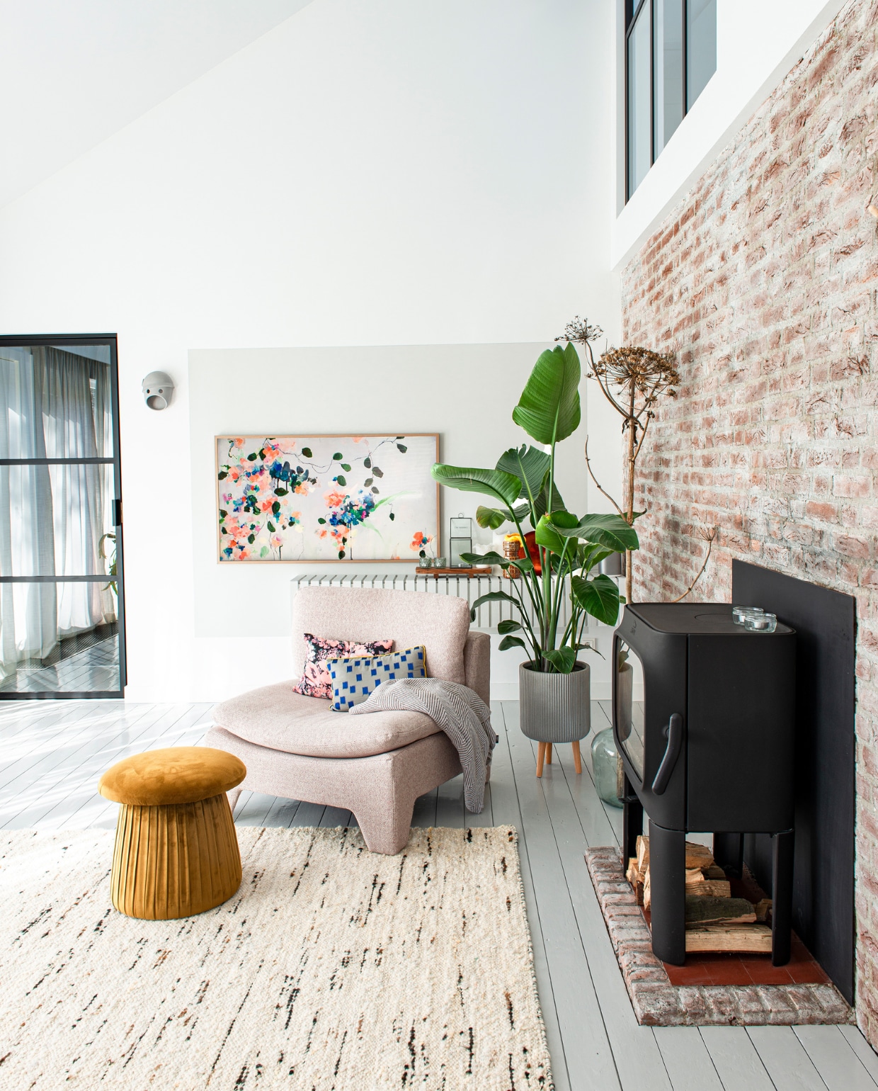 Stalen raam en deur Steellife. The Party Wall Lamp Coco van Moooi, plant met pot Intratuin. Televisie The Frame van Samsung, kader op de muur erachter kalkverf kleur parelwit van Kalk&amp;Co. Wandkast van latten zelfgemaakt en geschilderd met dezelfde kalkverf als het wandvlak. Fauteuil, kussens en vloerkleed  HKliving. Poef Mushroom van Sissy-Boy. Houtkachel Jøtul van Nijhof. vtwonen special DIY 6-2022 | productie De Binnenkijkers | styling Jeske Weel | fotografie Caroline Coehorst