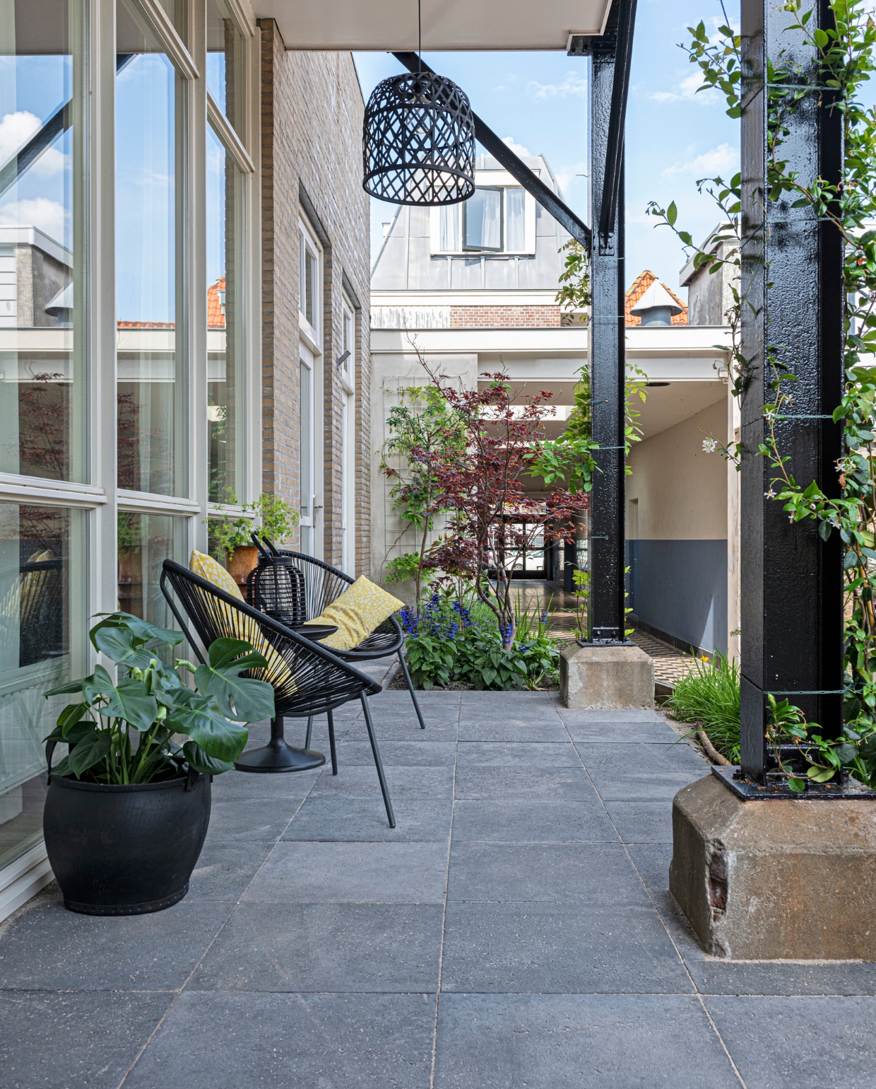 Het terras voor het huis. Stoelen Karwei, kussens Ikea, hanglamp Kwantum, rubberen mand Household Hardware. Tegels Koornneef De Lier. vtwonen binnenkijkspecial 12-2020 | styling Sharon Roest | fotografie Caroline Martinot