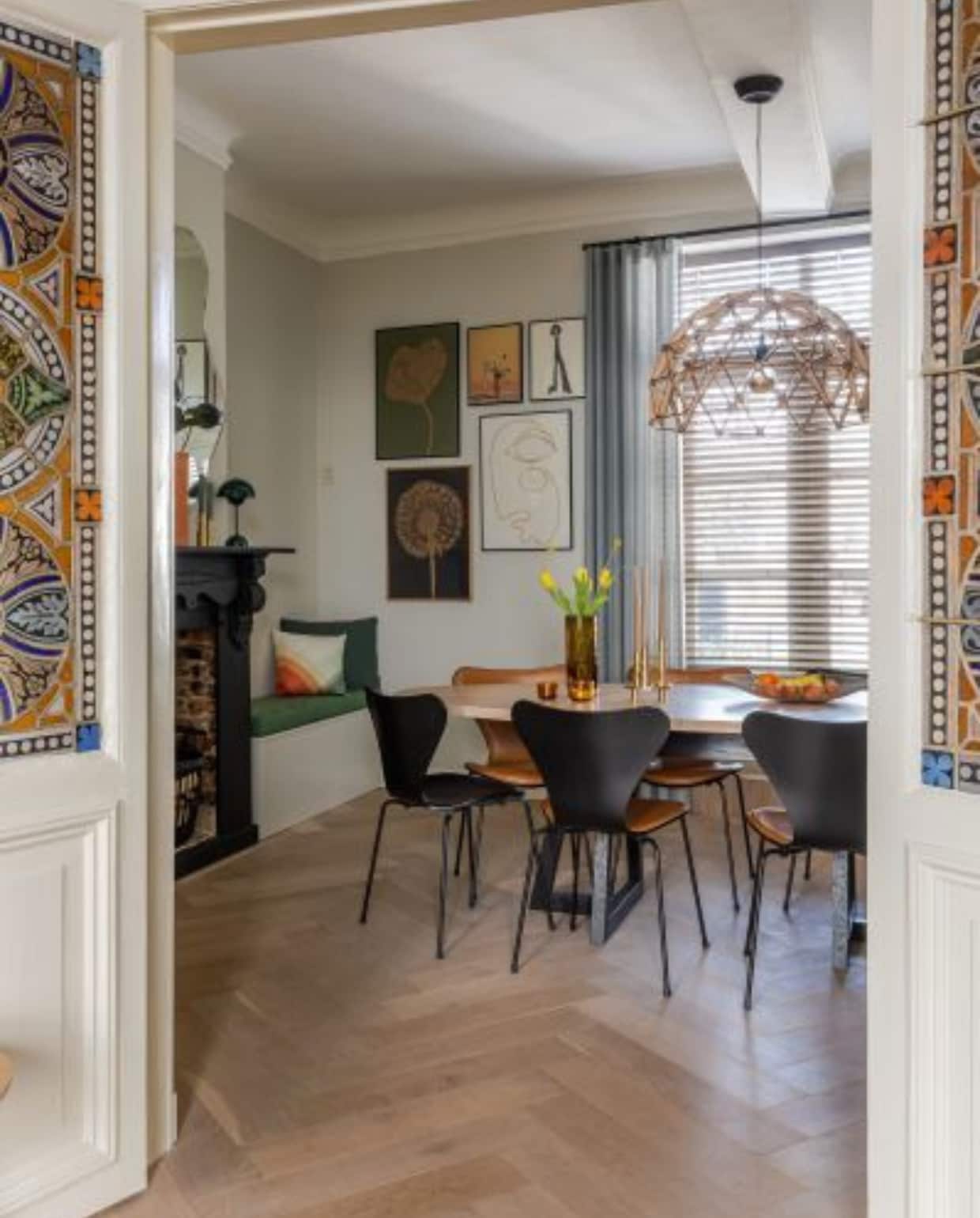 Houten visgraatvloer vtwonen. Vaas op schouw Muuto, spiegel Ferm Living, tafellamp &amp;Tradition. Tafel Slowwood, glazen vaas H&amp;M Home, waxinelichthouders Hema, fruitschaal Serax, eetkamerstoelen en kandelaars Fritz Hansen. Inbouwbank met groene matraskussens op maat gemaakt door Loft76, groen kussen Hay, gekleurd kussen Vitra. Prints Monika Petersen en Paper Collective. Gordijnen en jaloezieën De Kluis Thorn. Hanglamp Binthout. vtwonen special binnenkijken 12-2023 | productie Cocofeatures | fotografie Anne den Haan