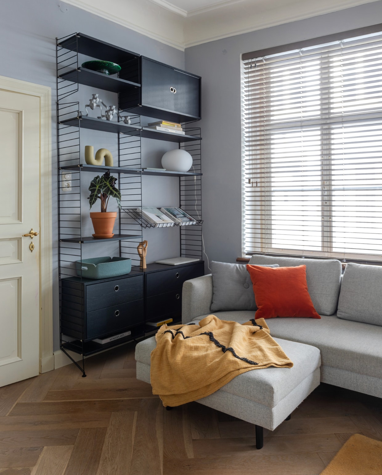 Muurverf Beton van Flexa. Houten visgraatvloer vtwonen. Bank Eyye. Kast String Furniture. Vloerkleed Aytm. Plaid, groene schaal en olijfgroene vaas HKliving. Kussens en hand Hay. Grijze kandelaar en groene mand Muuto. Bollamp Bga. Marmeren dienblad H&amp;M Home. Overig onbekend. vtwonen special binnenkijken 12-2023 | productie Cocofeatures | fotografie Anne den Haan