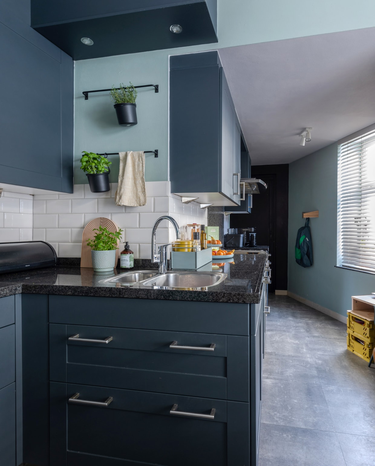 Muurverf Early Dew van Flexa. Keuken van vorige bewoners. Hangpotten en plafondlampen Ikea. Broodtrommel Brabantia, snijplank Hay, kruidenpot Dille &amp; Kamille, theedoek Casa, plantenbak Ferm Living. Kapstok Woodendot. Kratten Kwantum. Overig onbekend. vtwonen special binnenkijken 12-2023 | productie Cocofeatures | fotografie Anne den Haan