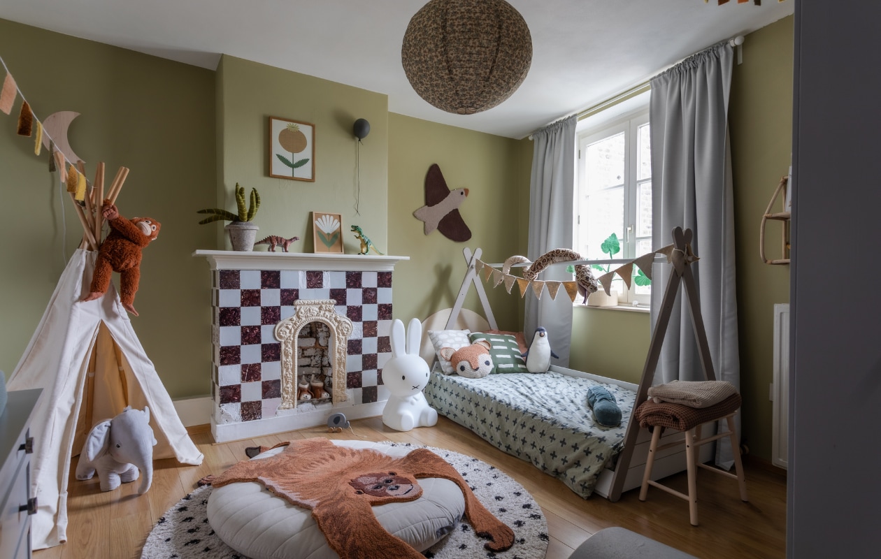 Muurverf Cardamom Skin van Lab Paint. Schouw met tegels origineel. Gordijnen, tipi, vloerkussen, kruk, slang en knuffelaap Ikea. Bed Je Eigen Kamer. Dekbedovertrek Hema. Kussens Fine Little Day en H&amp;M Home. Bruine sprei Vandyck, beige sprei, pinguïn, olifant en krokodil H&amp;M Home. Planten en vlaggenslinger KidsDepot. Nijntje-lamp Mr Maria.  Vloerkleed Volero. Hanglamp Konges Sløjd. Gekleurde slinger Juffrouw Duurzaam, wandlamp maan Hout is Prachtig, schilderijen Maa-noo, ballon ByOn, dino’s Action, wanddecoratie vogel Meri-Lou. Houten trekdier Little Dutch, sloffen Vintage Atelier. Overig onbekend. vtwonen special binnenkijken 12-2023 | productie Cocofeatures | fotografie Anne den Haan