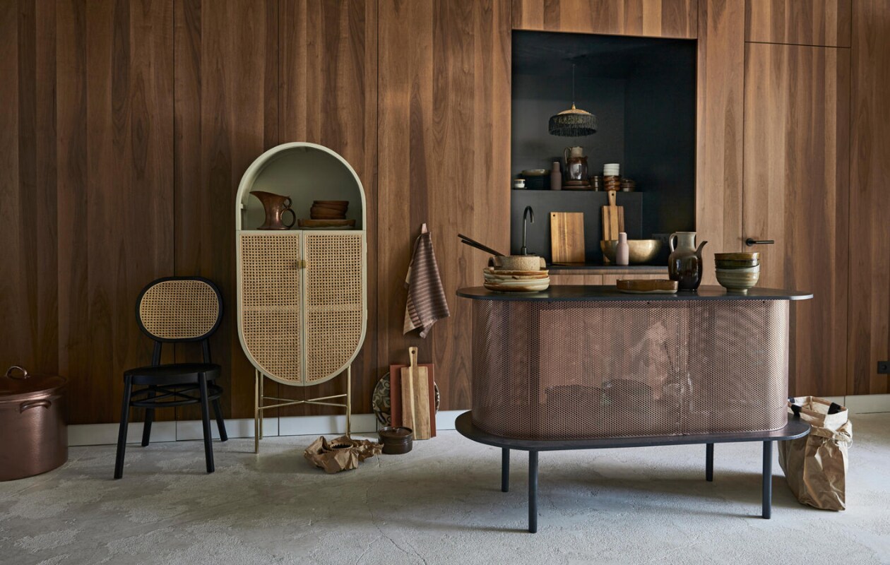 Wandbekleding en interieurontwerp door Sander van Eyck (cocoon-living.nl). Ovaal keukeneiland, op maat gemaakt, grote koperen pan (Combitex). Ovale kast, zwarte stoel met geweven rug, aardewerken kan, borden Kyoto, Ø 26 cm, grote kommen Kyoto (HK Living). Oranje snijplank van Hay, theedoek van Ferm Living, bruine rechthoekige schalen van Serax, zout- en peperstel van Menu (&amp;klevering). Lampje met raffia, rond dienblad, raffia schalen (MaisonNL). Keramieken schaal met deksel, zandkleurige schaal op borden, oude snijplanken, koperen kan (cocooncollectables.nl). Bronzen schaal, Ø 39 cm (X + L). Overig privébezit. vtwonen 08-2019 | styling Cleo Scheulderman | fotografie Jeroen van der Spek