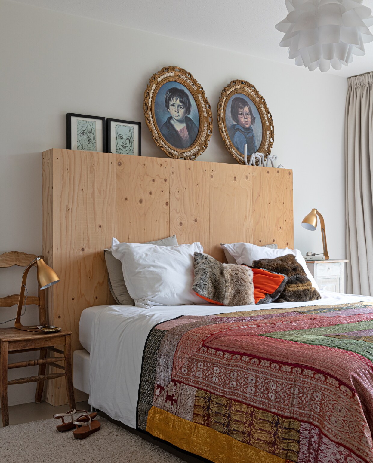 Muurkleur Ral 9010. Hanglamp en bed Ikea. Ombouw hoofdbord en tekeningen boven bed eigen ontwerp. Zigeuner- schilderijen rommelmarkt, houten stoel antiekwinkel. Lampjes Barefoot van Leitmotiv. Kussens zelfgemaakt, sprei uit Portugal. Marmoleumvloer Walton van Forbo vloeren. Gordijnen Hema. vtwonen 04-2021 | styling Sharon Roest | fotografie Caroline Martinot