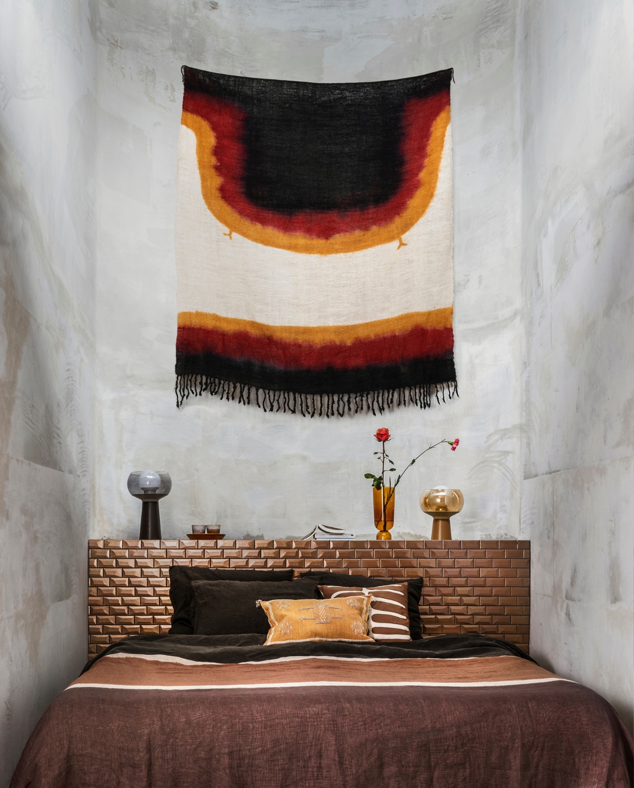 Wollen, met de hand geverfd wandkleed (householdhardware.nl). Linnen dekbedovertrek van Chivasso (jab.de). Bruin-wit kussen, kussen met borduursel (zenza.nl). Op bed een kanoko, ofwel een linnen tie-dye doek van Osborne &amp; Little (wva.nl). Lampen Mushroom van BePureHome, vaas van Hay, mokken van HKliving (vtwonen.nl). vtwonen 02-2022 | styling Marianne Luning | fotografie Stan Koolen