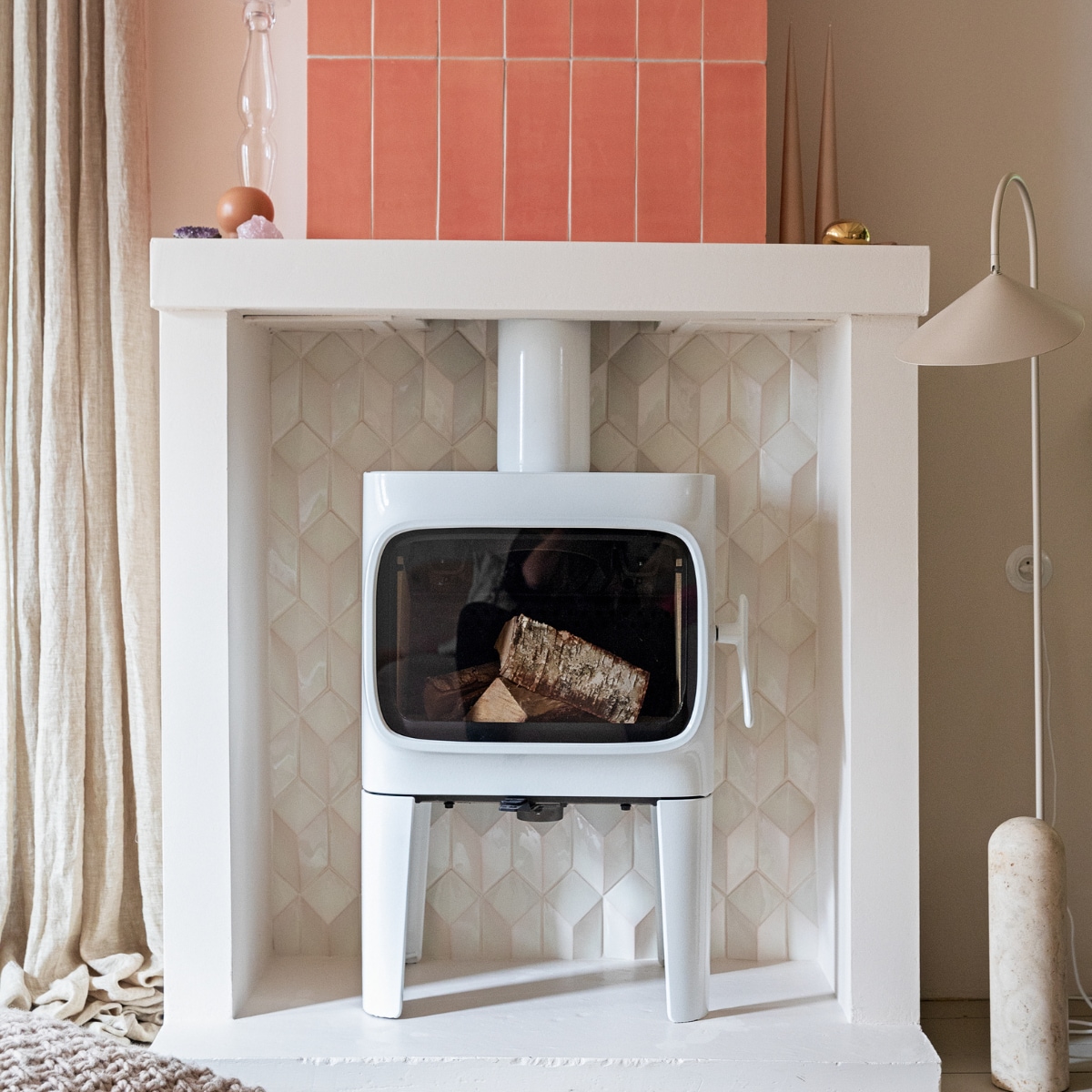 uitgelichte afbeelding. Houtkachel Jotul F305. Tegels 1030 cm kleur Flamingo Baby en witte tegels Constellation kleur Eggshell White via Quintalisque. Kussen Sukha. Lamp en kiezel Ferm Living. Glazen kandelaar herkomst onbekend. Kaarsen Ester &amp; Erik. vtwonen 02-2022 | styling Ilona Jongepier | fotografie Dana van Leeuwen