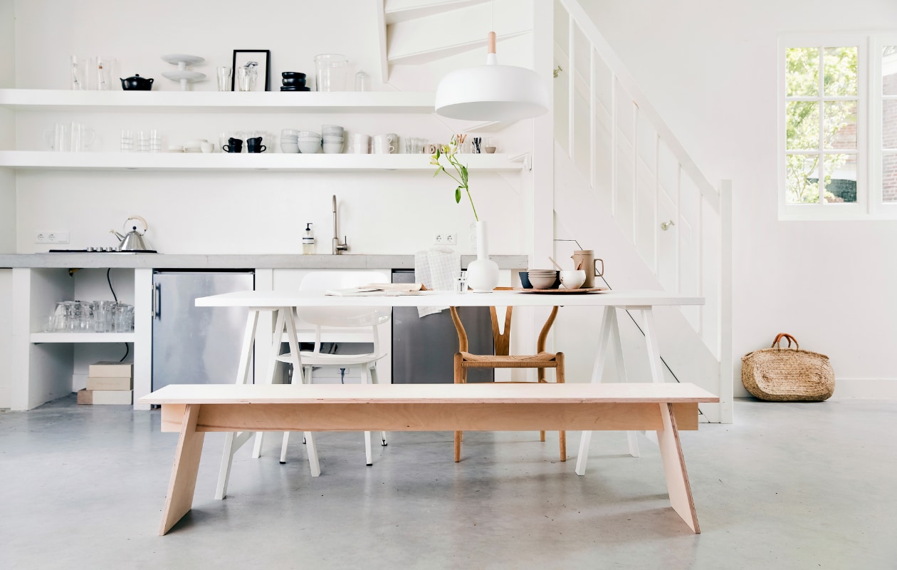 Bankje DIY, Tafel onderstel Brace in wit geschilderd essenhout van vtwonen, tafelblad Panel in wit geschilderd essenhout van vtwonen 190x80 cm, hanglamp Northern Acorn van Nordic Nest, witte vaas Muses Clio van Ferm Living, houten vogel S, tafellamp Milk van &amp;tradition, kandelaar Balance van Ferm Living (vtwonen.nl). Houten stoel Wishbone van Carl Hansen, witte stoel Revolt van Ahrend (misterdesign.nl). Porseleinen theepot van Hasami (thefinestore.com). Theedoek (hm.com). Bord met reliëfdruk plant (studioharmenelke.nl). Print van Loulou Avenue (loods5.nl). Overig privébezit. vtwonen 07-2019 | styling Kim van Rossenberg | fotografie Ernie Enkelaar