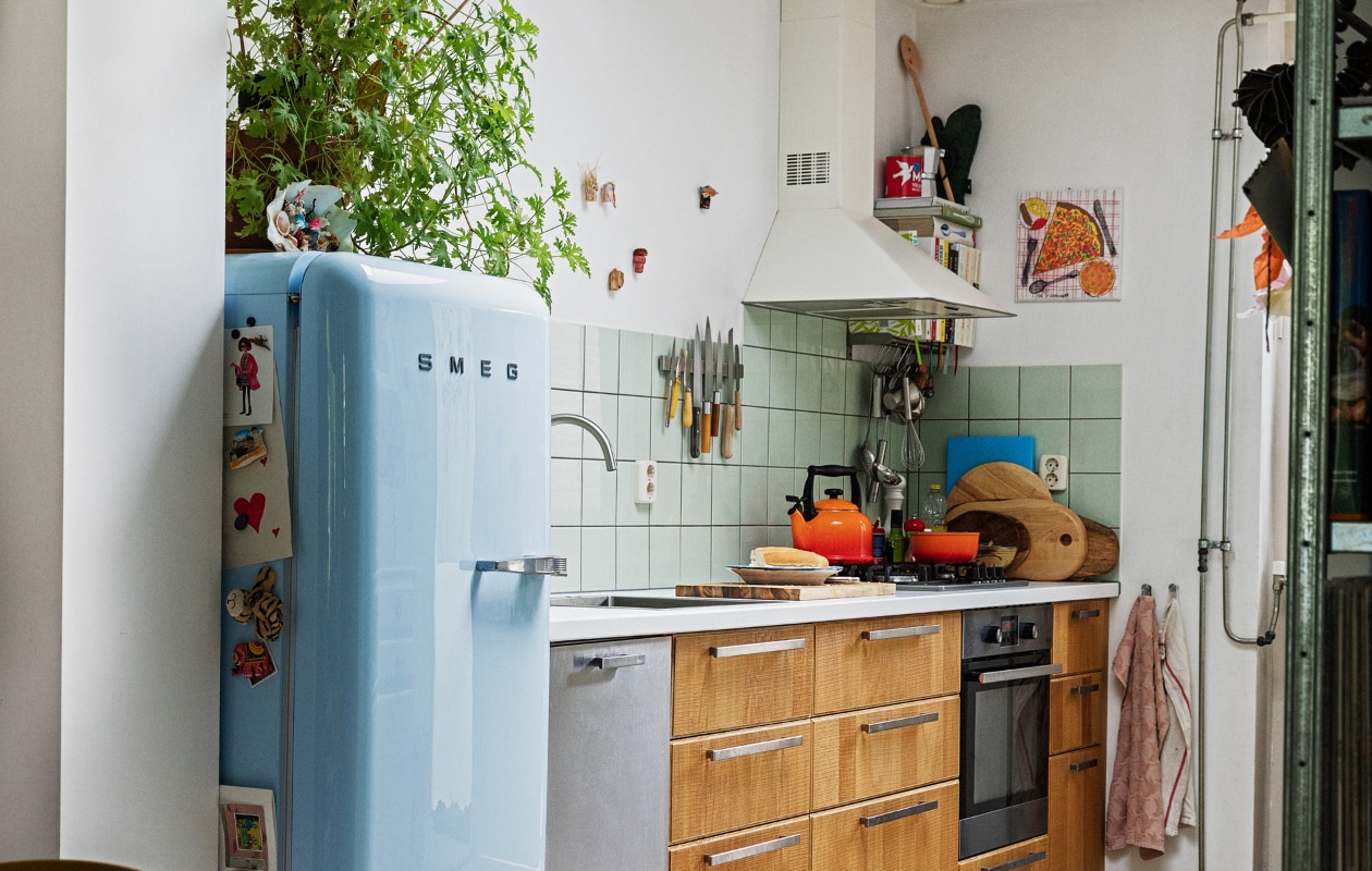Koelkast Smeg. Geraniumplant zelf gestekt. Kitsch schelp op koelkast souvenir uit Griekenland. Magneet-souvenirs meegenomen van verschillende reizen. Fluitketel en pan Le Creuset. Messen Suncraft, Opinel, Dille &amp; Kamille, Pallarès Solsona. Snijplanken Hay, Ikea, Serax. Soeplepel Brabantia. Rvs keukengerei Dille &amp; Kamille. Schaaltje van een pottenbakkersmarkt. Afzuigkap en oven Ikea. Ovenhandschoen Kook. Pollepel Kookhuis aan de Maes. Handdoeken Sissy-Boy. Tapijt The Souks. Pizza-schilderij Oskar. Ronde plafondlamp lampenwinkel.nl. vtwonen 13-2021 | styling Ilona Jongepier | fotografie Dana van Leeuwen