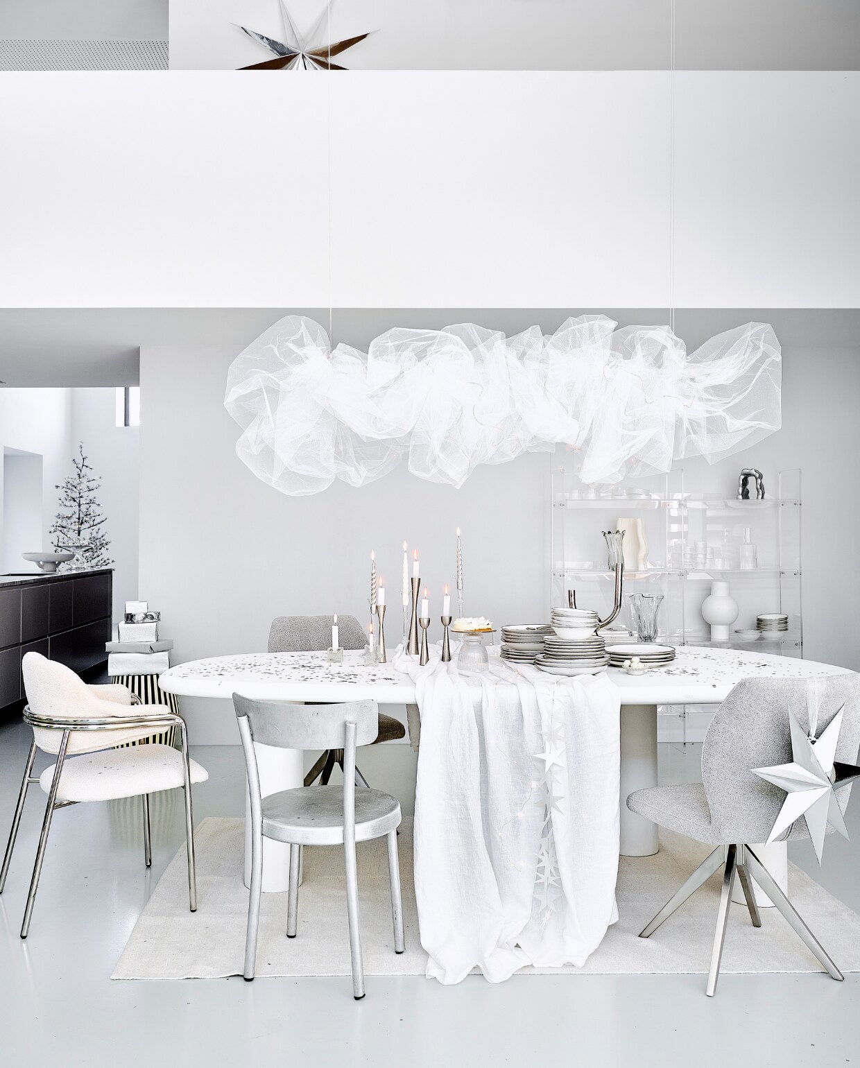 Eetkamertafel Bloomstone, mdf met lichte ecoplaster finish, 230x117x78 cm (bxdxh) € 1530,- (richmondinteriors.nl). Acryl vakkenkast 137x27,8x160 cm (bxdxh) € 1195,-, matwitte vaas € 49,95 (hkliving.com). Witte eetkamerstoel Albert Chair, teddystof en staal, 56x59x84 cm (bxdxh) € 605,30, verchroomde kandelaar € 87,25, zwart-witte bijzettafel, mdf en  mangohout, 41x41x48 cm € 530,30, glazen taartplateaus € 41,67, glazen vaas € 106,06 (nordal.com). Aluminium eetkamerstoel € 680,- (framacph.com). Grijze eetkamerstoel, polyester en staal € 229,- (jesperhome.com). Glazen ster, vierkante kandelaar, per stuk € 22,50 (alltheluckintheworld.nl). Servies van vtwonen vanaf € 7,95, metalen kandelaars, 16 cm € 16,95, 20 cm € 19,95 en 25,5 cm € 24,95, zilveren ster van papier, 110 cm € 29,95, ster 48 cm € 14,95, bestek Montreux van Sola, 50-delig € 115,99, schaal Earth van Serax, papier en pulp € 146,-, glazen etagère Damo van Ferm Living € 239,- (vtwonen.nl/shop). In kast: aluminium ornament € 135,-, geribbelde karaf € 39,-, geribbelde glazen van Ferm Living, set van 4 € 39,-, geribbeld glazen schaaltje van Ferm Living, set van 4 € 59,-, witte vaas Moire van Ferm Living € 139,-, glazen vaas Holo van Ferm Living € 71,99 (vtwonen.nl/shop). Linnen tafelkleed € 69,99, vloerkleed, 160x230 cm € 199,-, glazen kandelaars vanaf € 9,99 (zarahome.com). Gedraaide kaarsen, set van 6 € 15,95 (kunstindustrien.dk). Witte kaarsen € 1,- (hema.nl). Aardewerken schaal € 5,99 (hm.com). Kerstboom Alfi Tree van Sirius, 150 ledlampjes, 180 cm (h) € 275,-, papieren sterrenslinger van Räder € 16,95, lichtsnoer bloemen € 32,50 (two-gether.nl). Zilveren confetti € 9,20 (partywinkel.nl). Inpakpapier € 2,95 (vliegerpapier.nl). vtwonen bijlage kerst 2023 | styling Kim van Rossenberg | fotografie Sjoerd Eickmans