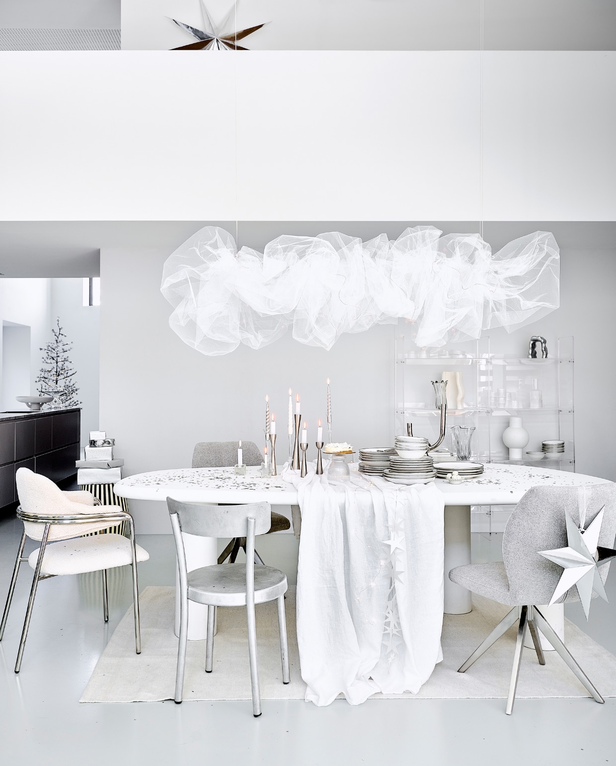Eetkamertafel Bloomstone, mdf met lichte ecoplaster finish, 230x117x78 cm (bxdxh) € 1530,- (richmondinteriors.nl). Acryl vakkenkast 137x27,8x160 cm (bxdxh) € 1195,-, matwitte vaas € 49,95 (hkliving.com). Witte eetkamerstoel Albert Chair, teddystof en staal, 56x59x84 cm (bxdxh) € 605,30, verchroomde kandelaar € 87,25, zwart-witte bijzettafel, mdf en  mangohout, 41x41x48 cm € 530,30, glazen taartplateaus € 41,67, glazen vaas € 106,06 (nordal.com). Aluminium eetkamerstoel € 680,- (framacph.com). Grijze eetkamerstoel, polyester en staal € 229,- (jesperhome.com). Glazen ster, vierkante kandelaar, per stuk € 22,50 (alltheluckintheworld.nl). Servies van vtwonen vanaf € 7,95, metalen kandelaars, 16 cm € 16,95, 20 cm € 19,95 en 25,5 cm € 24,95, zilveren ster van papier, 110 cm € 29,95, ster 48 cm € 14,95, bestek Montreux van Sola, 50-delig € 115,99, schaal Earth van Serax, papier en pulp € 146,-, glazen etagère Damo van Ferm Living € 239,- (vtwonen.nl/shop). In kast: aluminium ornament € 135,-, geribbelde karaf € 39,-, geribbelde glazen van Ferm Living, set van 4 € 39,-, geribbeld glazen schaaltje van Ferm Living, set van 4 € 59,-, witte vaas Moire van Ferm Living € 139,-, glazen vaas Holo van Ferm Living € 71,99 (vtwonen.nl/shop). Linnen tafelkleed € 69,99, vloerkleed, 160x230 cm € 199,-, glazen kandelaars vanaf € 9,99 (zarahome.com). Gedraaide kaarsen, set van 6 € 15,95 (kunstindustrien.dk). Witte kaarsen € 1,- (hema.nl). Aardewerken schaal € 5,99 (hm.com). Kerstboom Alfi Tree van Sirius, 150 ledlampjes, 180 cm (h) € 275,-, papieren sterrenslinger van Räder € 16,95, lichtsnoer bloemen € 32,50 (two-gether.nl). Zilveren confetti € 9,20 (partywinkel.nl). Inpakpapier € 2,95 (vliegerpapier.nl). vtwonen bijlage kerst 2023 | styling Kim van Rossenberg | fotografie Sjoerd Eickmans