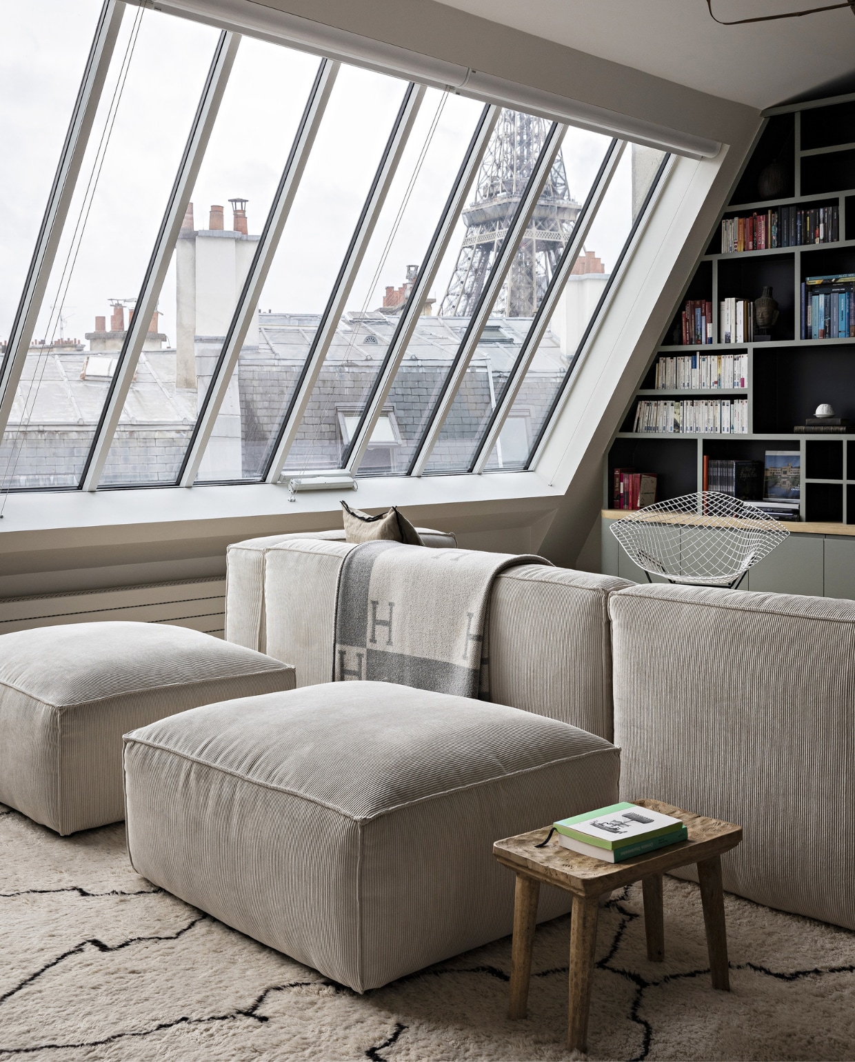 Bank La Redoute. Vloerkleed en plaid Mustapha Blaoui. Salontafel &amp;Tradition. Boekenkast en ramen op maat gemaakt. Hanglamp Ay Illuminate, stoel van Harry Bertoia voor Knoll. Poefs vlooienmarkt. Overig onbekend. vtwonen 12-2023 | productie AC Scoffoni | styling Marie-Maud Levron | fotografie Yann Deret | tekstbewerking Merel van der Lande