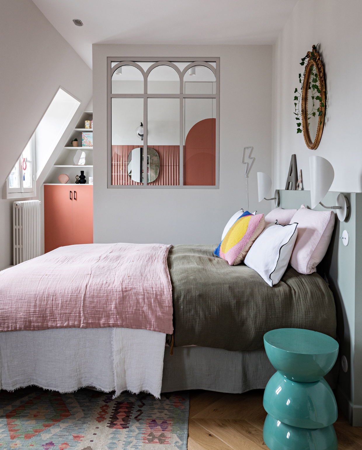 Spiegel boven bed erfstuk, vloerkleed Kilims Ada. Beddengoed La Redoute en Numero 74. Bedlampen Am.pm. Wandlamp bliksemflits en bed La Redoute, bijzettafel India Mahdavi, radiator Acova. Tussenraam ontworpen door Anne, gemaakt door Claustra. Verf hoofdbord Green Blue, verf kast en deur Red Earth van Farrow &amp; Ball. Overig onbekend. vtwonen 12-2023 | productie AC Scoffoni | styling Marie-Maud Levron | fotografie Yann Deret | tekstbewerking Merel van der Lande