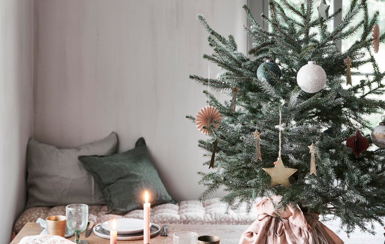 In de boom: papieren waaier, groene bal, bal met sneeuw, groene ster, honeycomb ornament (intratuin.nl). Messing vallende sterren (weldaad.com). Grote messing ster van Madam Stoltz (deens.nl). Op tafel: servet (sostrenegrene.com), waxinelichthouder (intratuin.nl). Messing beker, kandelaar in stervorm (weldaad.com). Groen wijnglas van Nordal (deens.nl). Zitkussen Nisha rose 50x155 cm (lxb), groen kussen van Bungalow 50x50 cm (scandicliving.nl). Zachtgroene kussensloop 50x60 cm (yumeko.nl). vtwonen kerstbijlage 12-2020 | styling Marlies Does | fotografie Bart Brussee