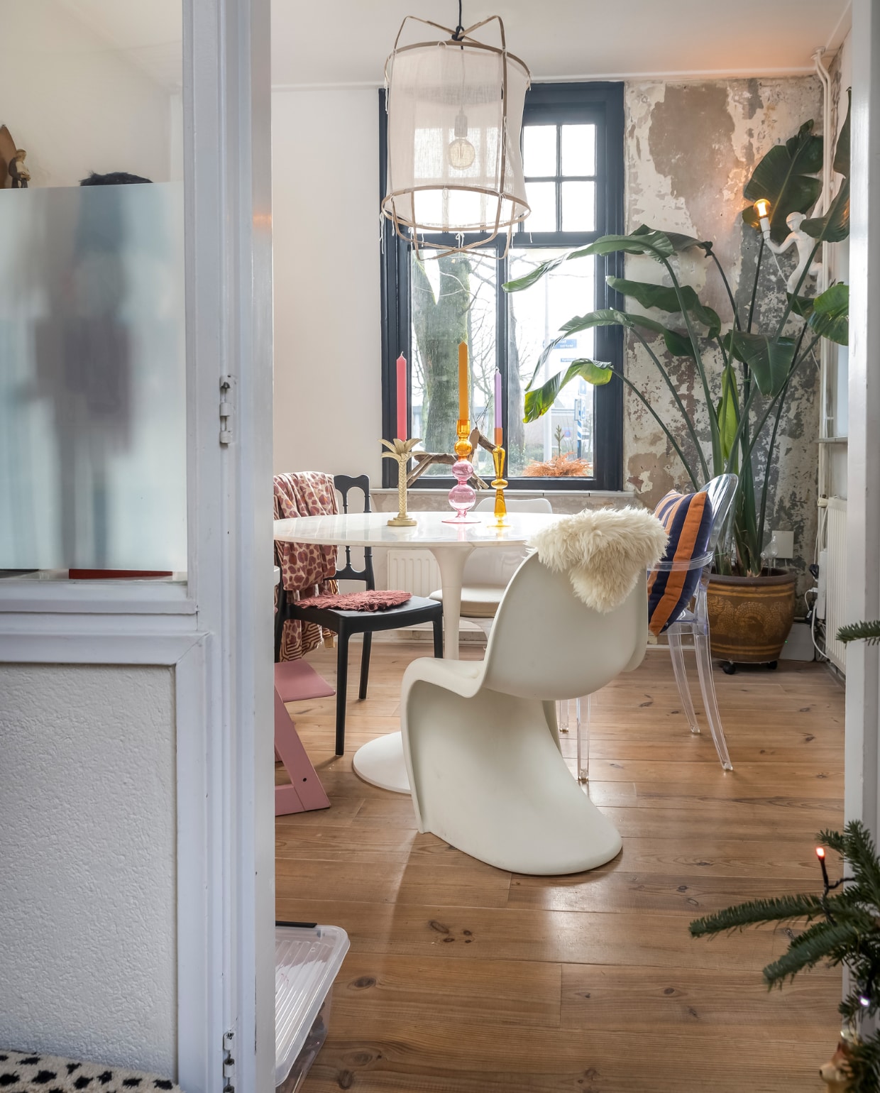 Eettafel Karwei. Hanglamp zelfgemaakt. Roze stoel Tripp Trapp van Stokke. Witte stoel Vitra. Zwarte stoel Loods 5. Transparante stoel Kartell. Gestreept kussen HKliving. Aaplamp Seletti. Kandelaars bladvorm en geel glas Kwantum. Kandelaar roze bollen Urban Nature. Kaarsen Puur Petra. Overig onbekend. vtwonen 13-2023 | fotografie Henny van Belkom