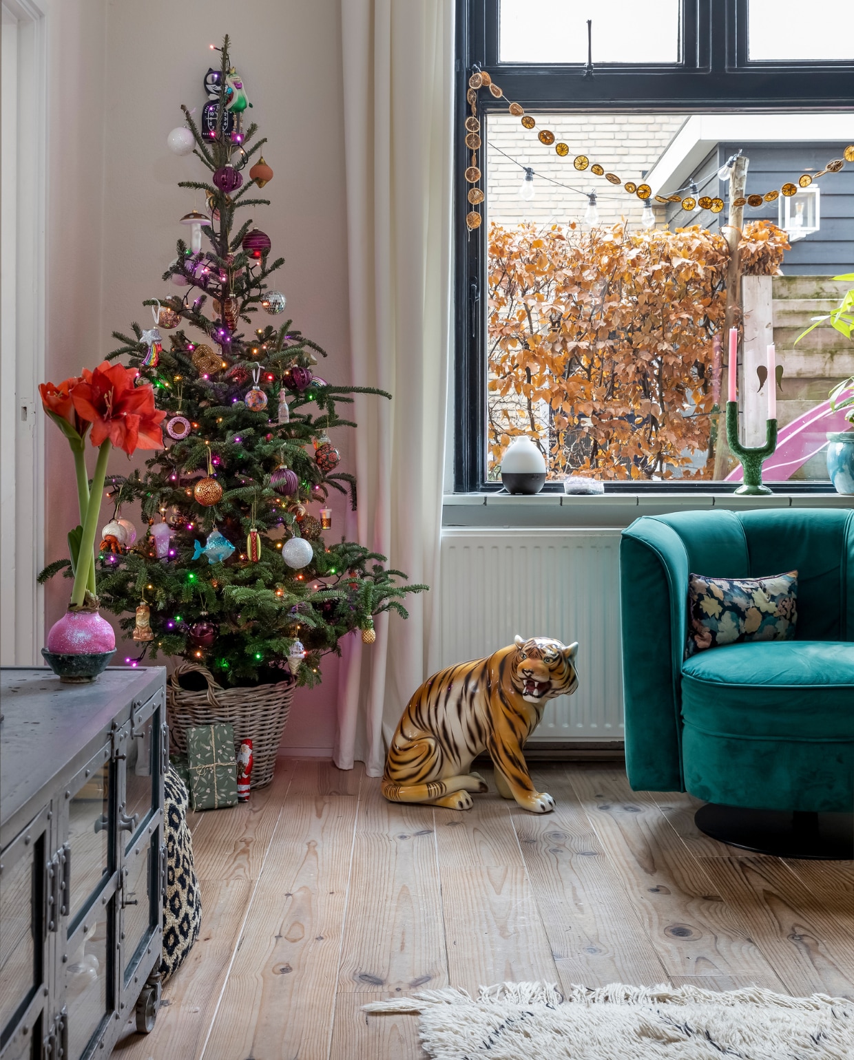 Mand en kerstboom Boomkwekerij Berkhof. Kerstballen o.a. Blokker en Søstrene Grene. Tijgerbeeld vintage. Zwart-witte vaas Geurwolkje. Groene kandelaar Bij Elles. Roze kaarsen Puur Petra. Blauwe vaas Intratuin. Gebloemd kussen HKliving. Sinaasappelslinger zelfgemaakt. Turquoise draaifauteuil Dutchbone. vtwonen 13-2023 | fotografie Henny van Belkom