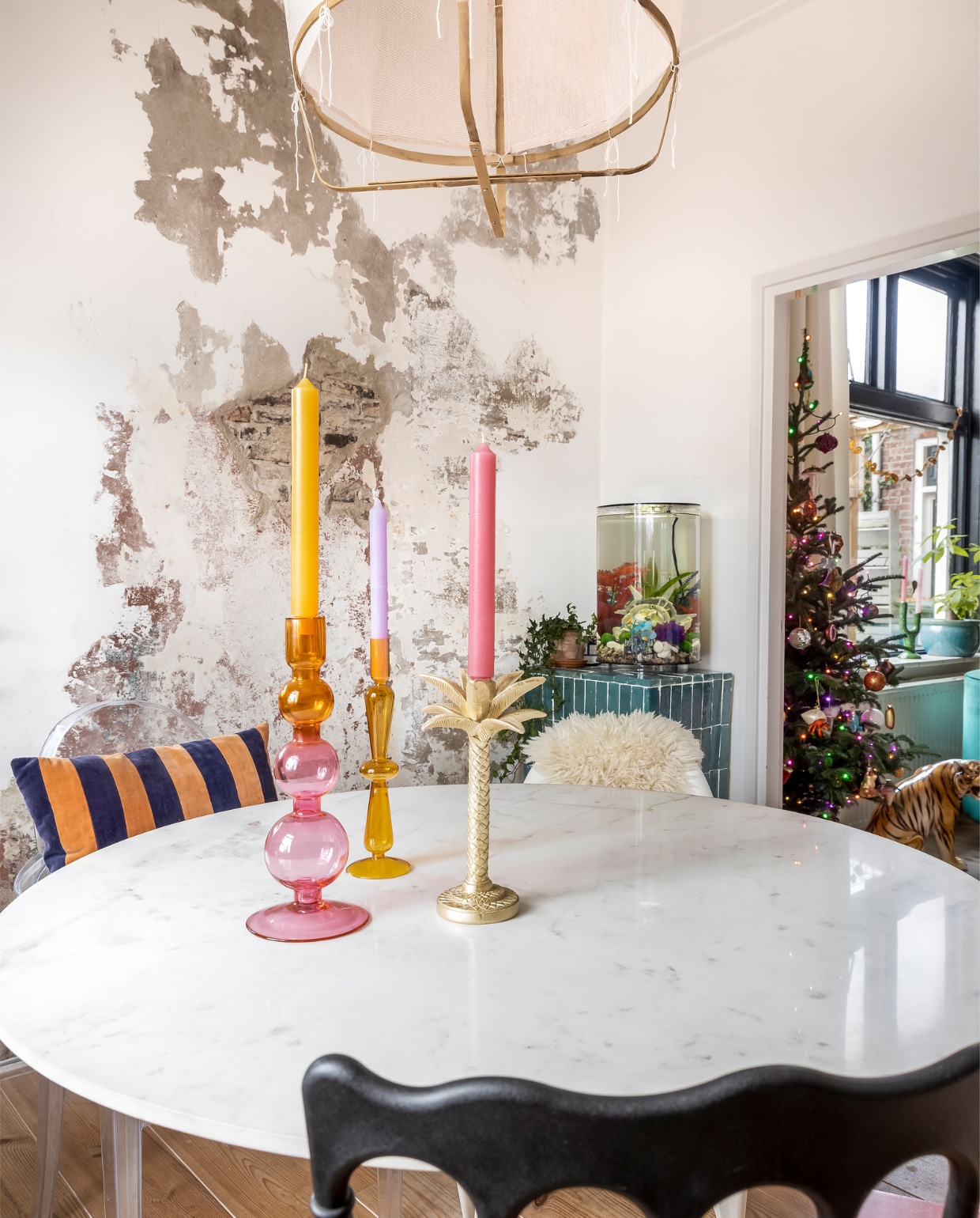 Aquarium Biorb. Voetstuk met Marokkaanse bejmats zelfgemaakt. Eettafel Karwei. Hanglamp zelfgemaakt. Zwarte stoel Loods 5. Transparante stoel Kartell. Gestreept kussen HKliving. Kandelaars bladvorm en geel glas Kwantum. Kandelaar roze bollen Urban Nature. Kaarsen Puur Petra. vtwonen 13-2023 | fotografie Henny van Belkom