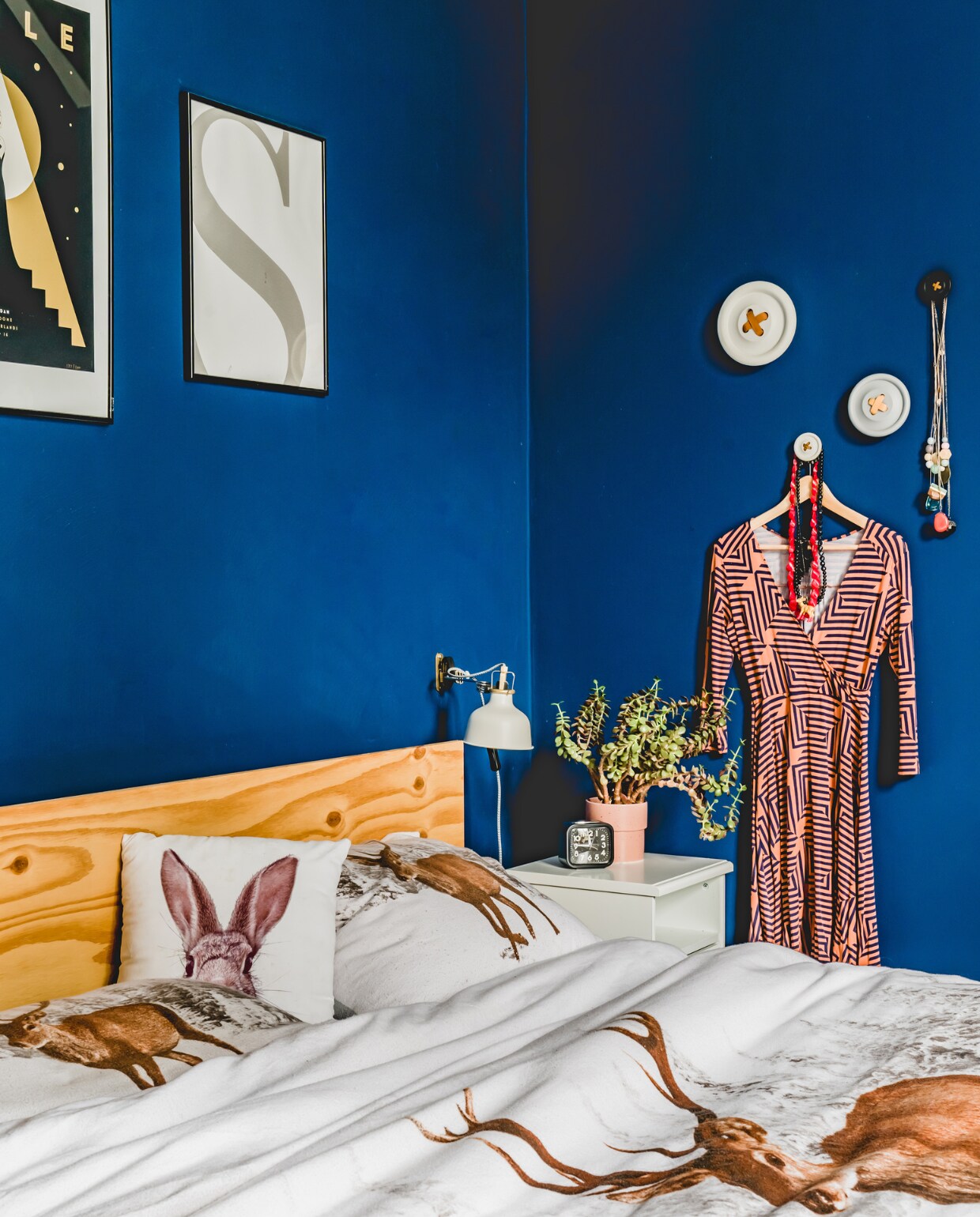 De slaapkamer is de enige kamer die niet licht van kleur is, de helderblauwe tint is kleur Jeans van Flexa. Het houten hoofdbord maakten ze zelf. Knopen aan de muur van HKliving, beddengoed met dierenprint van beddengoed.com. Aan de muur hangt rechts eigen werk van Marjolein en links een poster van Adele. Lamp en nachtkastje van Ikea. vtwonen 12-2019 | productie Features &amp; More | styling Wilma Custers | fotografie Ivar Janssen