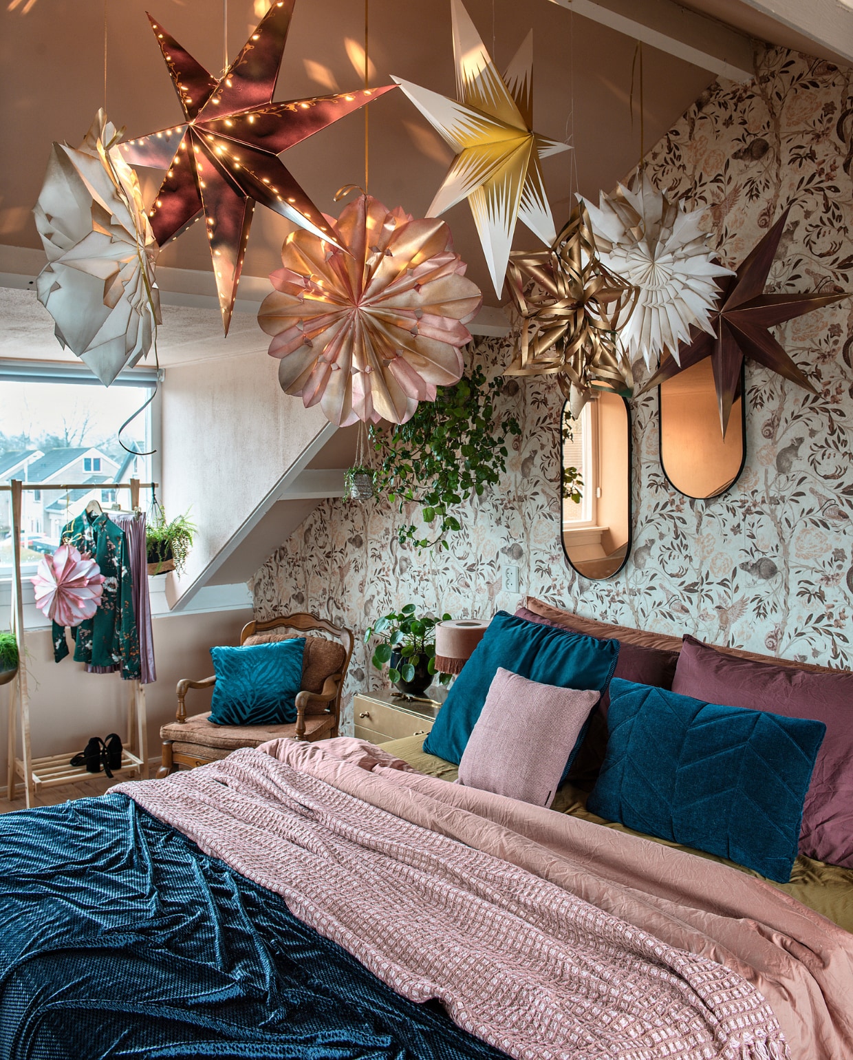 De kerststerren zijn van Ikea en zelfgemaakt met boterhamzakjes. Behang metratjesdessin Mineheart. Roze plaid en bedlinnen Suite 702. Spiegels en petrolsprei van stof van Kwantum. Kussens: op stoel onbekend, links Boer Staphorst,rechts Volt Studio, klein Jysk. Kastje en stoel kringloop. Lampje Skylerstore.Kledingrek Action, blouse Up to date mode, rok kringloop, schoenen H&amp;M. vtwonen 12-2020 | styling Mindy Schroor | fotografie Ton Bouwer | productie Monique van der Pauw