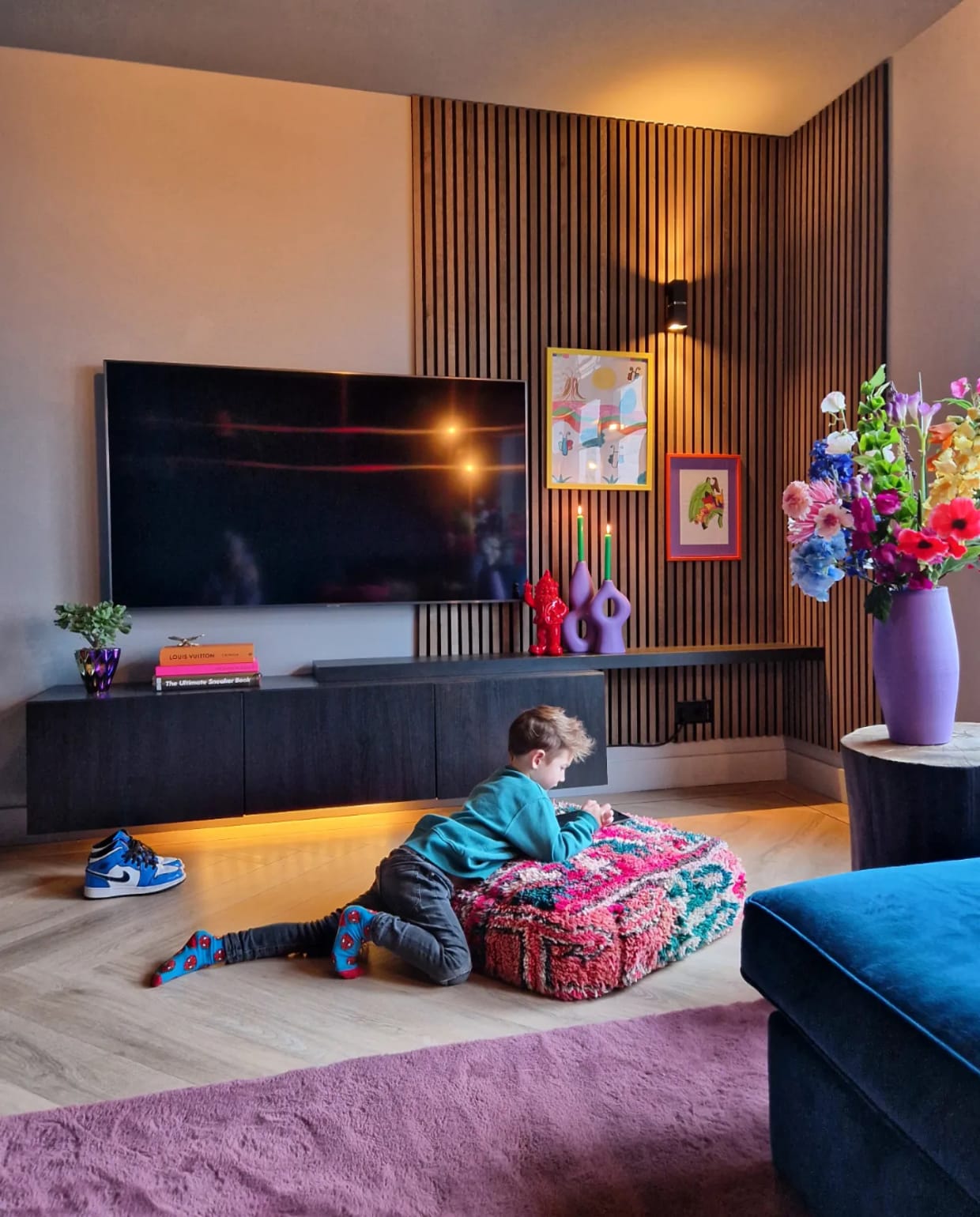 Akoestische wandpanelen WoodUpp, tv-meubel Ikea, boeken HKliving en Louis Vuitton, poef Living Maroc. Kandelaars Kwantum, geverfd. Vaas kringloop, geverfd. Wandlamp Lucide. Vloer walvisgraat van Floer, bank A-meubel. Overig onbekend. Fotografie Anne Marie Vandersteen