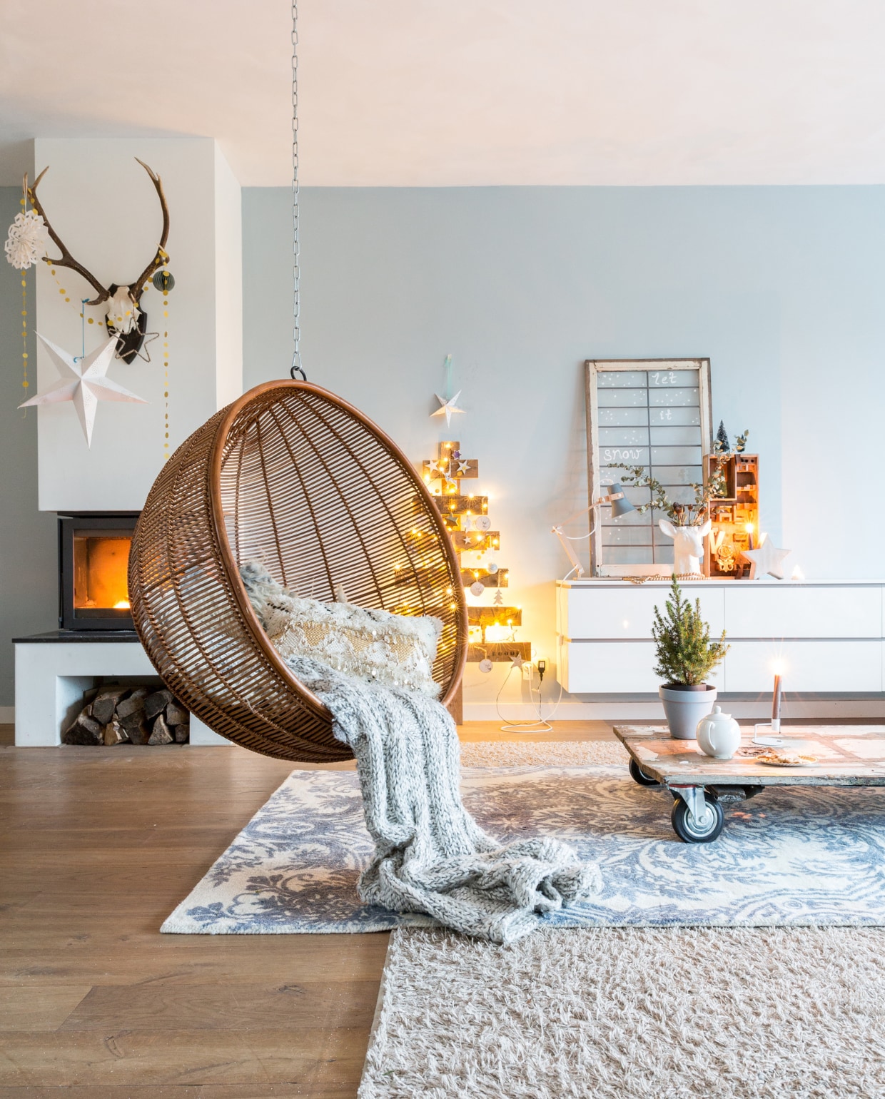 De houten kerstboom is een diy van houten pallets. Dressoir van Jann interieurs, een oud raam van Loods G dient als decoratie, hertenkop als vaas van Tuinland. Gewei boven de haard van de Oranjerie, okergeel slingertje Dille &amp; Kamille, witte ster van Tuinland. De salontafel is een oude deur op wielen en werd bij AnoukB gekocht. Het mini-boompje op tafel staat in een zelf geschilderd terra potje. Wandkleur Blue Grey van Painting the Past. Blauwwit kleed van Wehkamp, grijs kleed van Hornbach. vtwonen kerstspecial 2016 | fotografie Hans Mossel | styling Sabine Burkunk | tekst Seline Steba