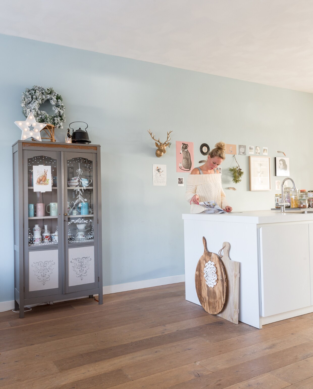 Met aan de ene kant het eetgedeelte en de andere kant de woonkamer zit de keuken praktisch in het midden van het huis. ‘Ideaal, want als je staat te koken, sta je altijd middenin de ruimte en word je overal bij betrokken.’ Keuken B1 van Bulthaup, servieskast (eigenlijk een boekenkast) van Smuk &amp; Chic, Sabine tekende met krijtstift sneeuwvlokjes, een mistletoe en teksten op de ruiten: ‘Een leuke en snelle diy en na de feestperiode was je het er zo weer af met water.’ Wit sterrenlichtje van Hema, houten broodplanken van Combitex. Wandkleur Blue Grey van Painting the Past. vtwonen Kerstspecial 2016 | fotografie Hans Mossel | styling Sabine Burkunk | tekst Seline Steba