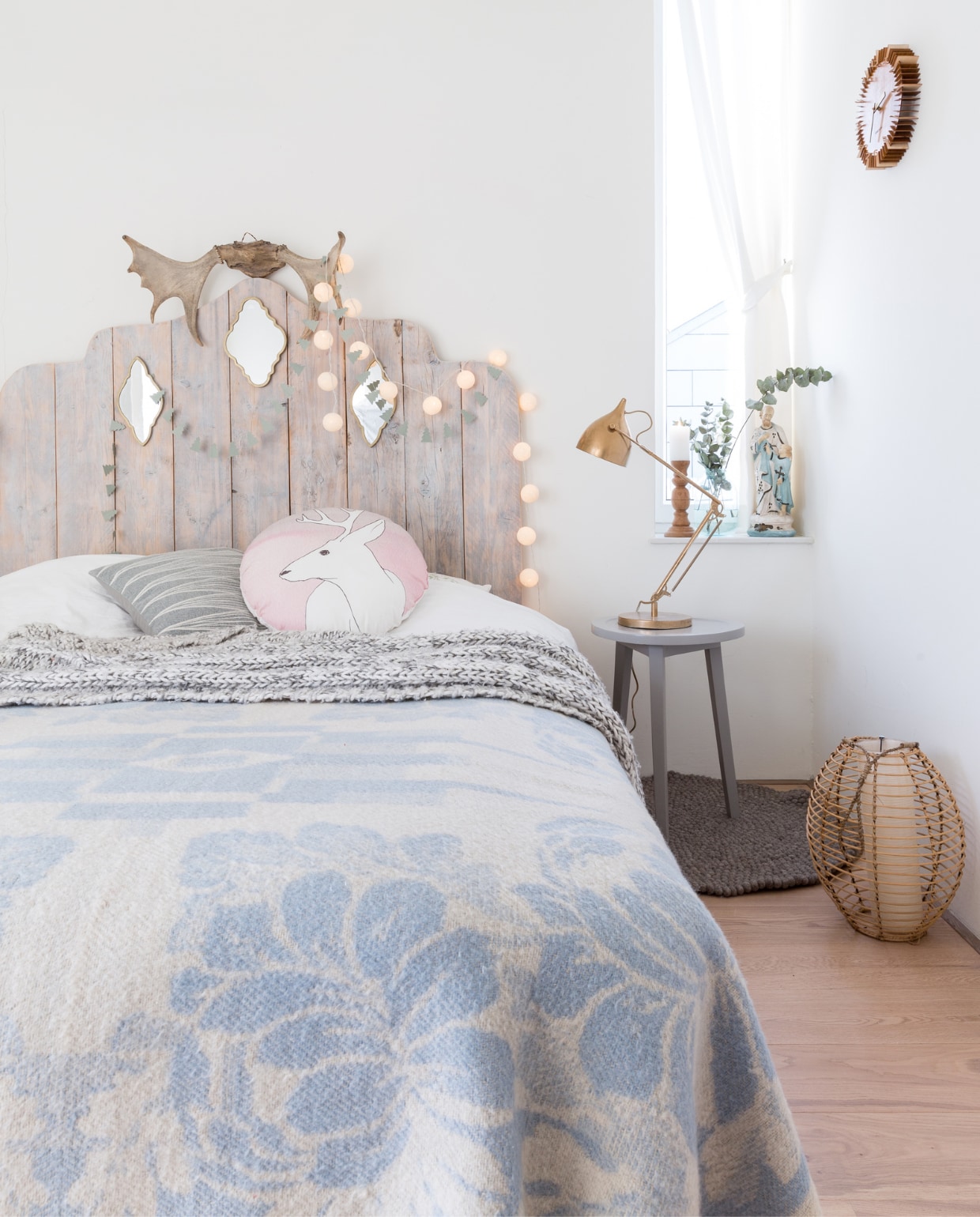 Het hoofdbord op de slaapkamer werd door Sabine getekend en op maat gemaakt door een timmerman. Spiegeltjes van Lifestyle, gewei van Loods G, slingertje Dille &amp; Kamille, lichtslinger van cottonballlights.com. De kruk naast het bed is van vtwonen.nl, de bureaulamp is van Zuiver en door Sabine koperkleurig gespoten. Rond vloerkleedje van Sukhi, klok Presenttime, lantaarn en blauwwitte deken van de kringloop, gebreide plaid Laif &amp; Nuver, kussens van House Doctor. vtwonen Kerstspecial 2016 | fotografie Hans Mossel | styling Sabine Burkunk | tekst Seline Steba