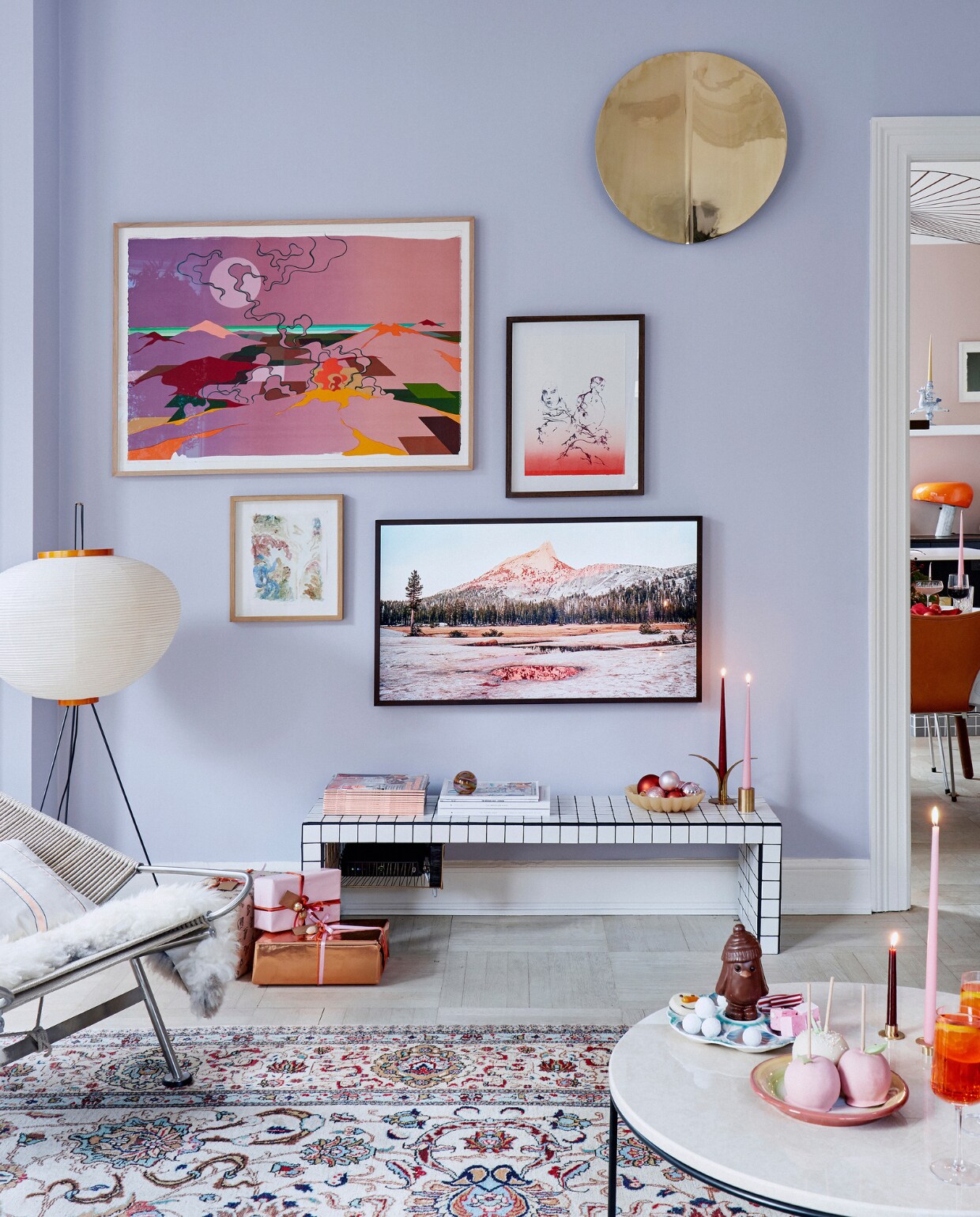 Muurverf s1510-r60b Jotun. Lamp Noguchi voor Vitra. Aan de muur hangen kunst van Eske Kath, Cathrine Raben Davidsen en Jakob Steen, een goudkleurig ornament van Yume en een Samsung The Frame tv. Herkomst witte bijzettafel onbekend, kaarsen Ester &amp; Erik. Chocola van Hotel Chocolat en kerstmarkten, oranje glazen Louise Roe. vtwonen kerstspecial 2020 | productie Living Inside | fotografie Martin Sølyst