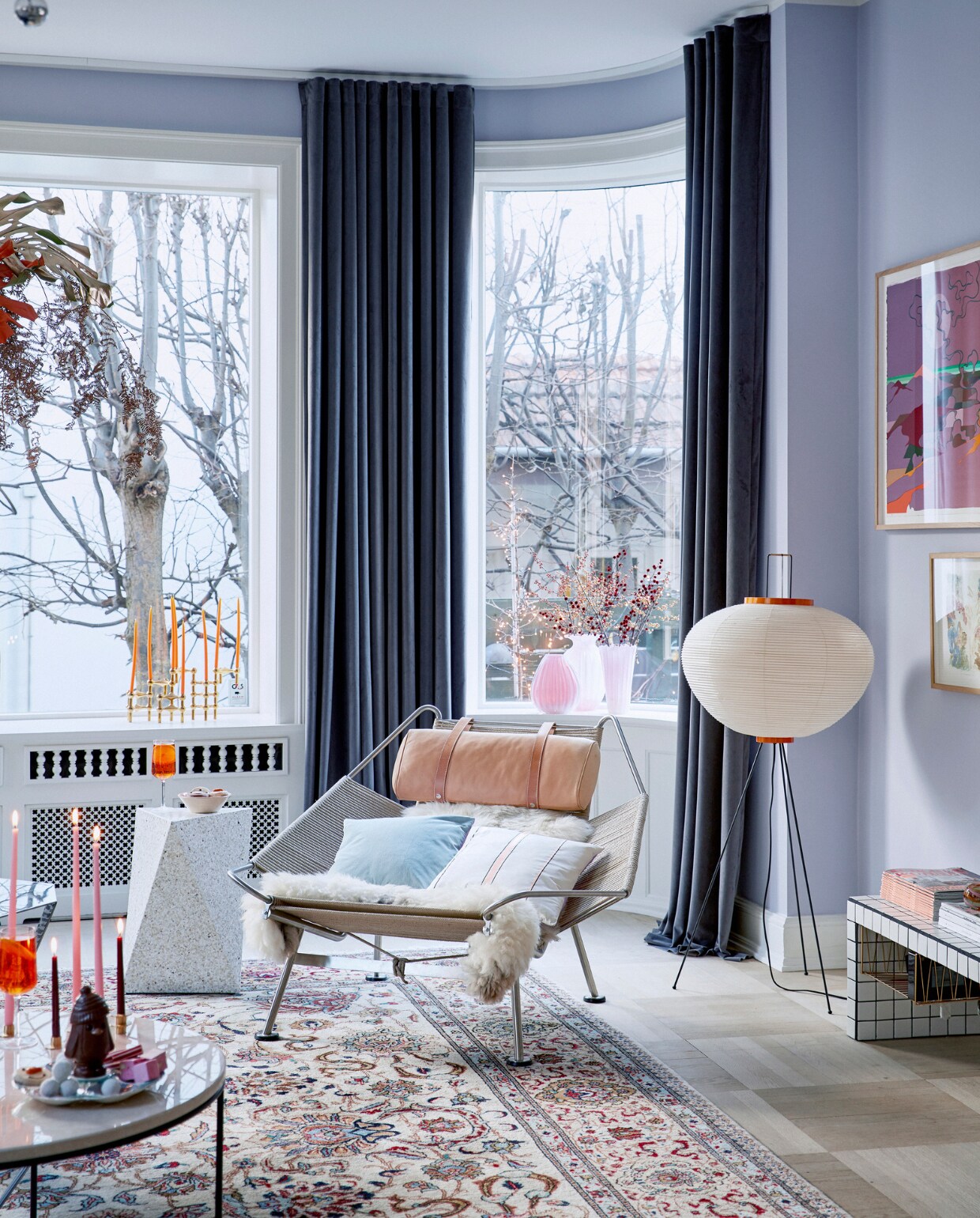 Muurverf s1510-r60b Jotun. Lamp Noguchi voor Vitra. Aan de muur hangt kunst van Eske Kath, Cathrine Raben Davidsen en Jakob Steen. Herkomst witte betegelde bijzettafel onbekend. Kaarsen en kaarshouders Ester &amp; Erik. Chocolade van Hotel Chocolat en kerstmarkten. Oranje glazen Louise Roe. Salontafel Planner Fritz Hansen. Hanglamp Sputnik Jolina. Vloerkleed erfstuk. Hangende decoratie zelfgemaakt. Stoel Flagline Hans Wegner. Witte bijzettafel Delta Yume. Muranoglas vazen in vensterbank vintage. vtwonen kerstspecial 2020 | productie Living Inside | fotografie Martin Sølyst