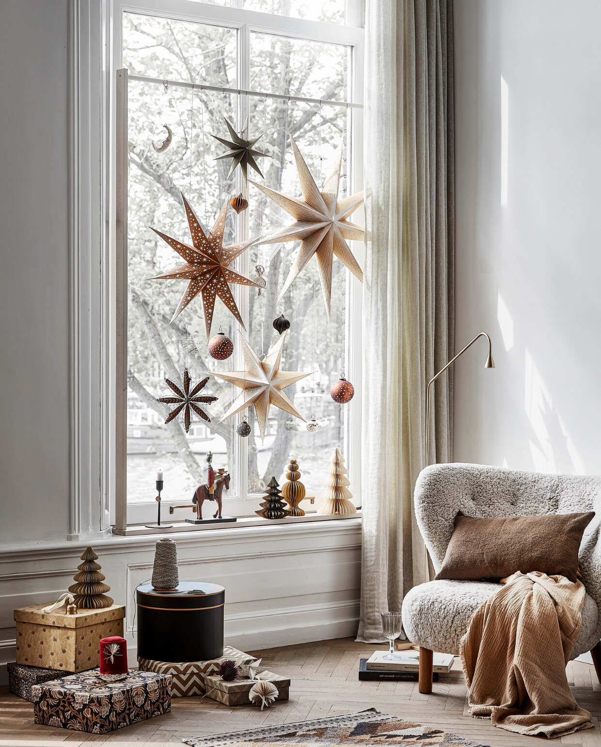Plaid, 140x190 cm € 59,99, vloerkleed 70x200 cm € 179,-, wijnglas € 3,99, bruin wollen kussen, 30x50 cm € 39,99 (zarahome.com). Vloerlamp Austère, brass € 899,- (thefinestore.com). Fauteuil Little Petra van schapenvacht met notenhouten poten € 4691,- (andtradition.com). Klein rood hoedje Red Soldier van Meri Meri € 22,50 (kinderfeestwinkel.nl). Papieren paddenstoelhanger, set van 2 € 19,-, goudkleurige hanger Dancing Ballerina € 10,-, goudkleurige hanger Moon € 10,-, papieren kerstbomen vanaf € 8,-, papieren ballerina, set van 2 € 19,50, papieren hanger Drops, set van 3 € 12,-, goudkleurig klokje € 10,-, papieren ster Cassiopeia, 90 cm € 35,-, papieren ster, 60 cm € 25,-, papieren ster Moonlight, 50 cm € 20,-, 80 cm € 35,-, papieren ster klein, set van 3 € 10,-, treasure box met dessin, set van 2 € 48,75, kandelaar 3 koningen, set van 3 € 270,- (bungalow.dk). Sneeuwvlok hanger € 15,50, handgemaakte koperkleurige kerstbal met stippen € 6,95, koperen kerstbal € 6,25, zwarte kandelaar M € 18,25 (weldaad.com). Boek Living Barefoot € 75,- (casagitane.com). Verf raamframe kleur Joanna (littlegreene.nl). Zwarte ronde doos, gordijnen privébezit. vtwonen 13-2022 | styling Kim van rossenberg | uitvoering Richard van Meerveld | fotografie Peggy Janssen