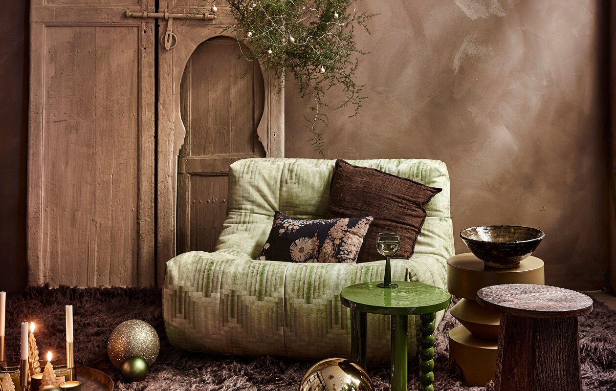 Fauteuil Lazy Lounge Chair, 105x105x75 cm (bxdxh), bruin hoogpolig vloerkleed Fluffy in Espresso, wol en katoen, 200x300 cm (hkliving.nl). Groene acaciahouten bijzettafel Hava, okergele metalen bijzettafel Bora, mangohouten bijzettafel Lux, keramieken theelicht, kerstboomkaarsjes (loods5.nl). Gouden kunststof kerstballen (kerstversiering.nl). Keramieken schaal op tafel (householdhardware.nl). Goudkleurige kandelaars laag, hoog (hema.nl). Groene glazen kerstbal, per 6 (bol.com). Gouden glazen kerstballen (xenos.nl). Krans zelfgemaakt. Overig privébezit. vtwonen 13-2023 | styling Moniek Visser | fotografie Peggy Janssen