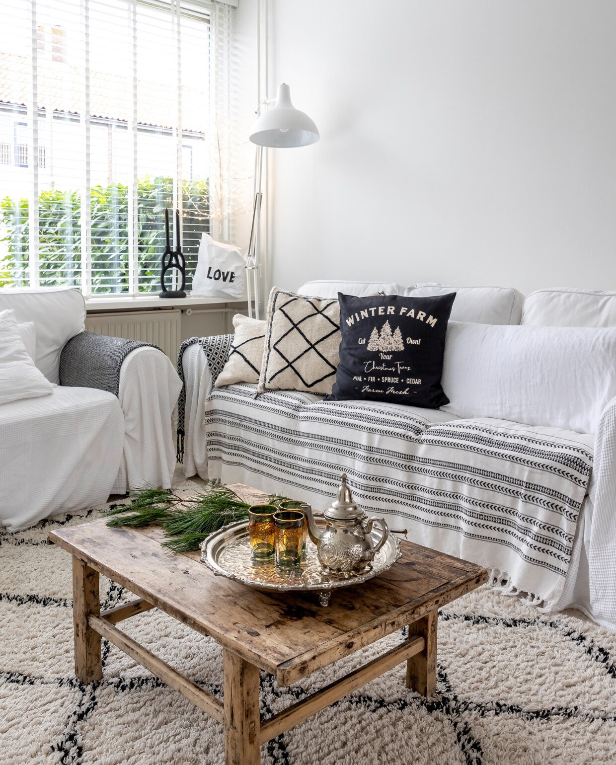 Bank Ektorp Ikea. Salontafel Rockanjeaanzee. Kleed Karwei. Staande lamp Fonq. Zwart-wit kussen uit Marrakech via Vinted. Kussens op bank en gestreepte plaid H&amp;M, witte plaid Ikea. Love tas en kandelaar Loftloft. Theepot en glazen kringloop. vtwonen 13-2023 | fotografie Henny van Belkom