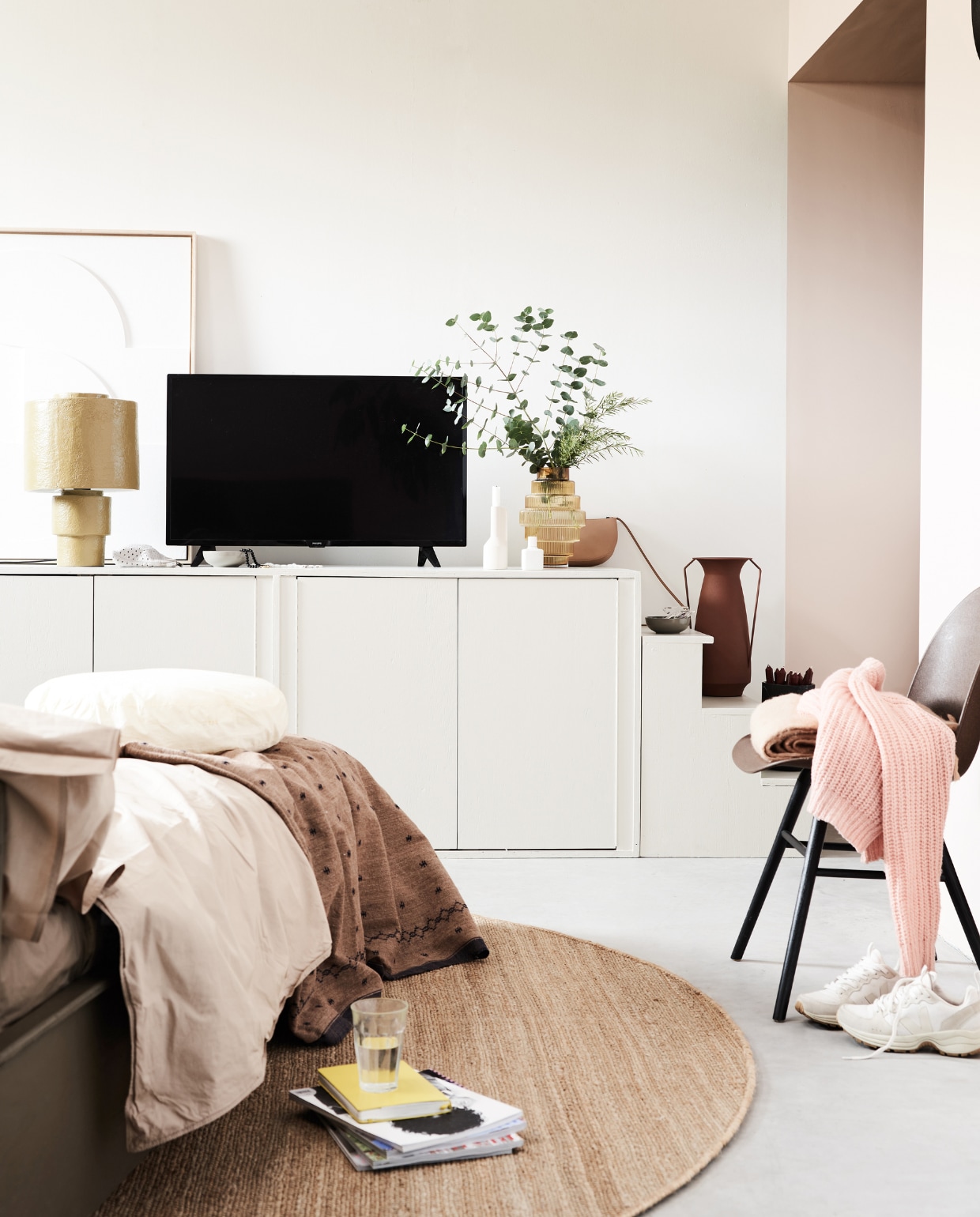 Houten kast en trap op maat gemaakt in kleur Shaded White 201 van Farrow &amp; Ball, vintage houten bed (combitex.nl). Mosterdkleurige tafellamp Gesso, 51x33 cm, hennep vloerkleed, 250 cm (Ø), vilten reliëfpaneel ingelijst, 83x4x103 cm (bxdxh) (hkliving.nl). Oranje glazen vaas Steps L van Pols Potten, bordeauxrode metalen vaas op trap van Bloomingville, 18x40 cm (Øxh) (vtwonen.nl). Stoel Albert Kuip, zwarte marmeren vaas Fajen (zuiver.nl) met kaarsen, per 10(hema.nl). Poederroze plaid, 130x170 cm (bxl) (maisonnl.com). Katoenen camelkleurig dekbedovertrek, 240x220 cm, katoenen camelkleurige kussenslopen, 60x70 cm, katoenen kussenhoes Bigdot kleur Smokey, 50x10 cm (Øxh), binnenkussen (suite702.nl). Handgemaakte beige wollen sprei Ekram, 170x235 cm (ottomania.nl). Overig privébezit. vtwonen 02-2022 | styling Esther Jostmeijer | fotografie Bart Brussee