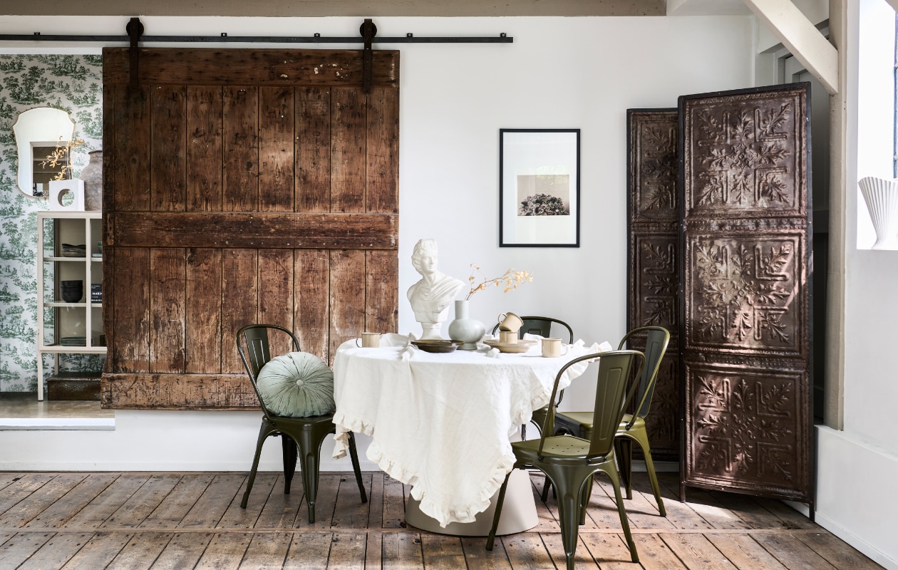 Mdf eettafel Jorre van Woood in Militair Brown, 120x76 cm (Øxh), ijzeren stoel Afternoon van vtwonen, porseleinen vaas Tank van BePureHome, velvet kussen Halo van BePureHome (basiclabel.nl). Metalen kamerscherm van oude plafonddecoratie, 188x2x194 cm (lxbxh) (hetkabinet.nl). Vintage borstbeeld (fortuneflea.com). Bekers en borden uit serviesset Yard Picnic in kleur Cashmere van Ferm Living, 8-delig, metalen borden uit picknickset Yard Picnic van Ferm Living in Cashmere en Olive, 8-delig (vtwonen.nl/shop). Overig privébezit. vtwonen 11-2023 | styling Marlies Does | fotografie Sjoerd Eickmans
